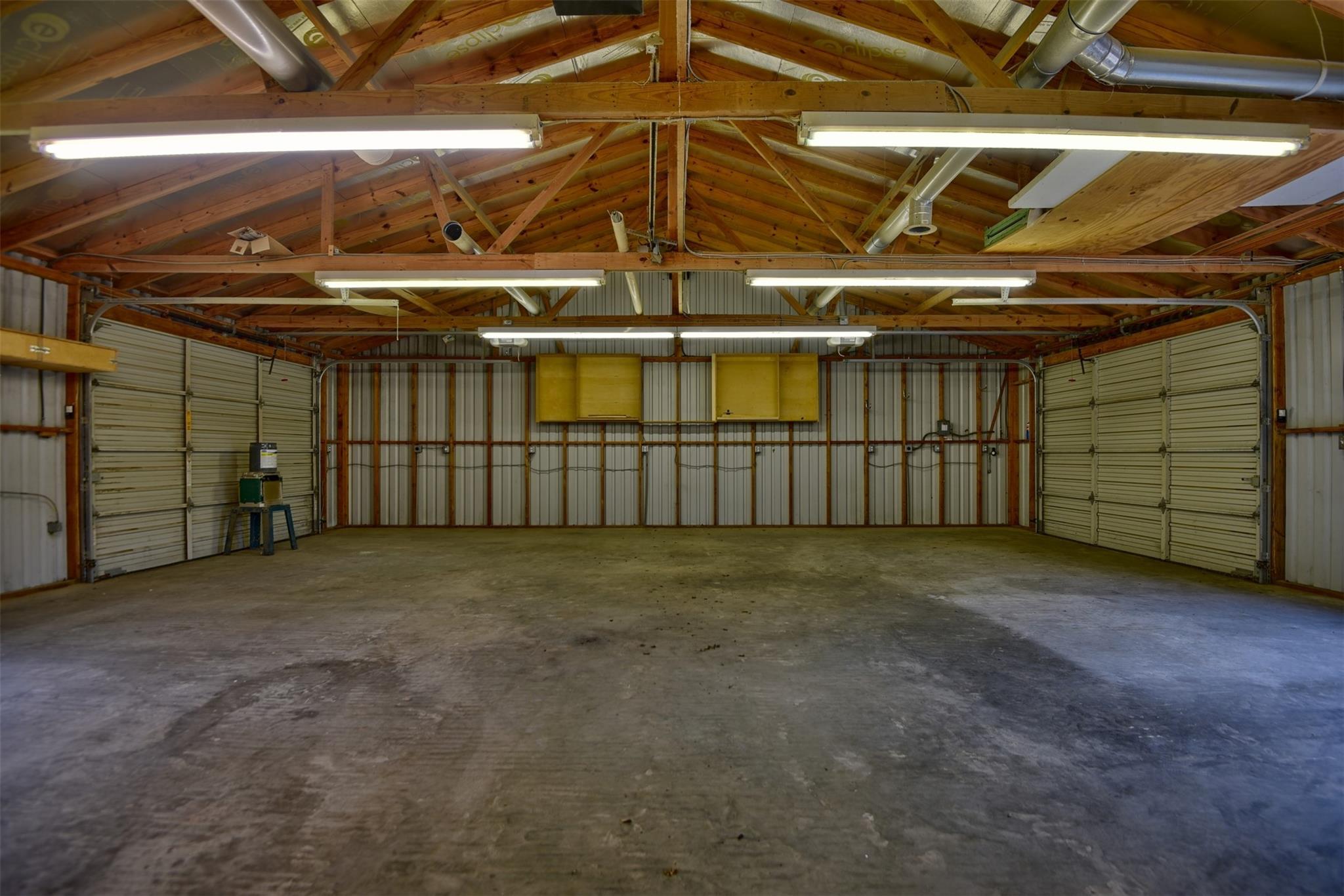 Large empty garage with concrete floor, multiple roll-up doors, and exposed wooden roof trusses.