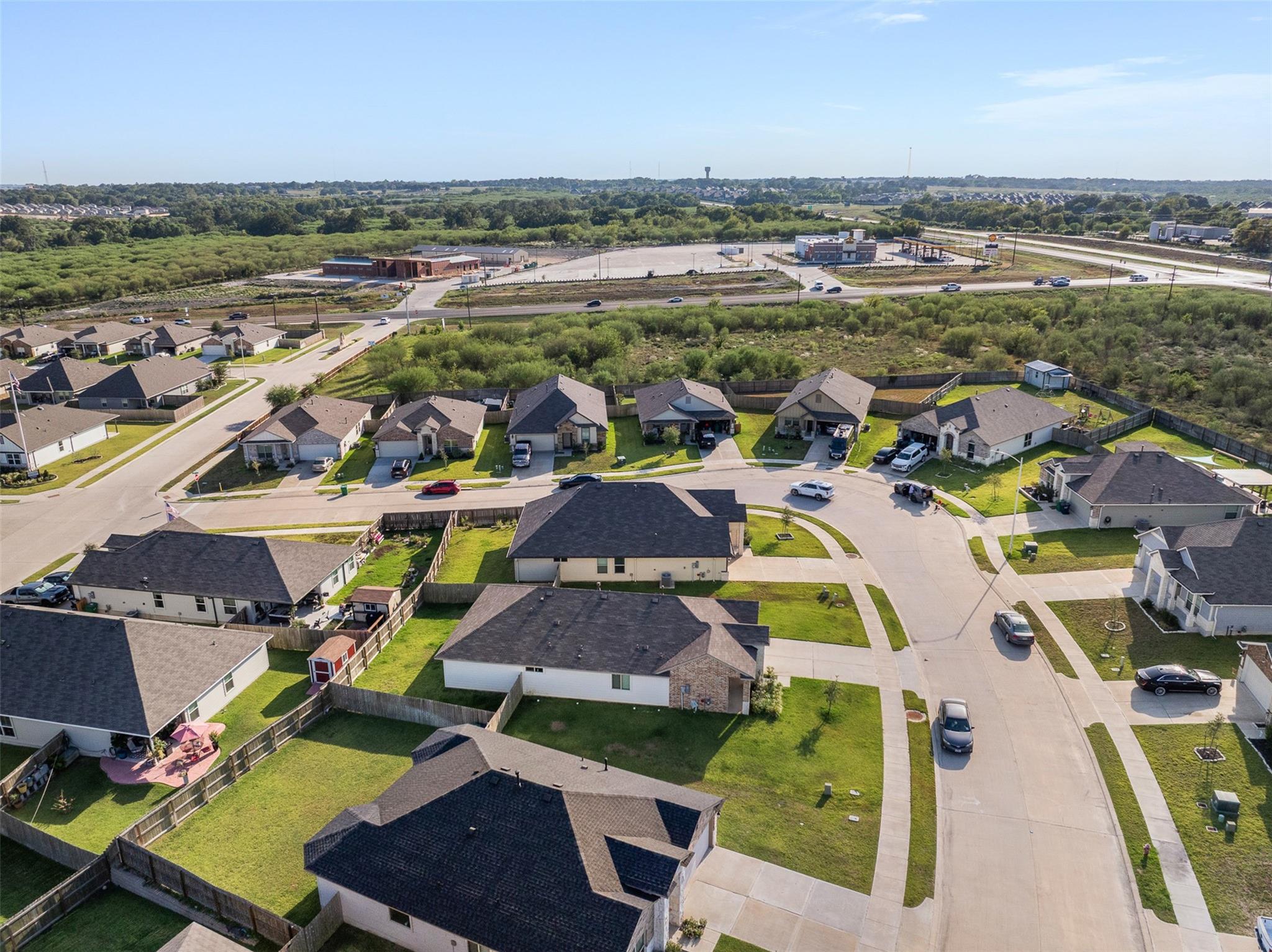 Aerial view of a residential neighborhood with fenced yards and a highway in the distance.