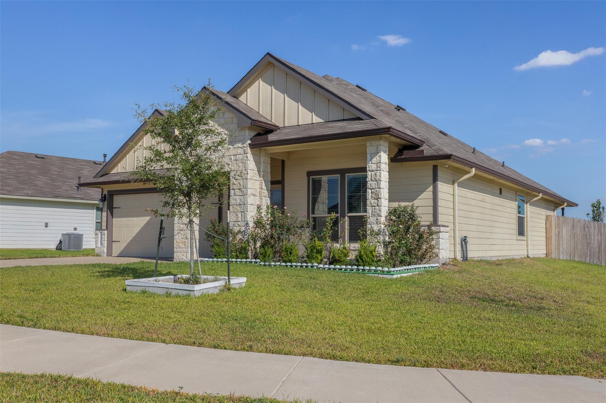Beige single-story house with stone porch columns, attached garage, and landscaped front lawn.