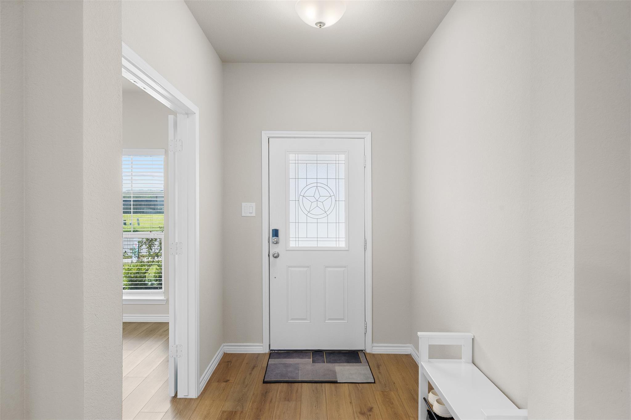 Entry foyer with a white front door featuring decorative glass and a narrow bench.
