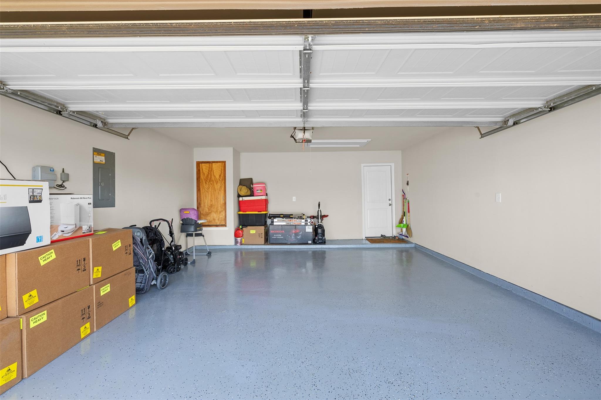 Spacious garage with a speckled floor, raised overhead door, and storage boxes along one side.