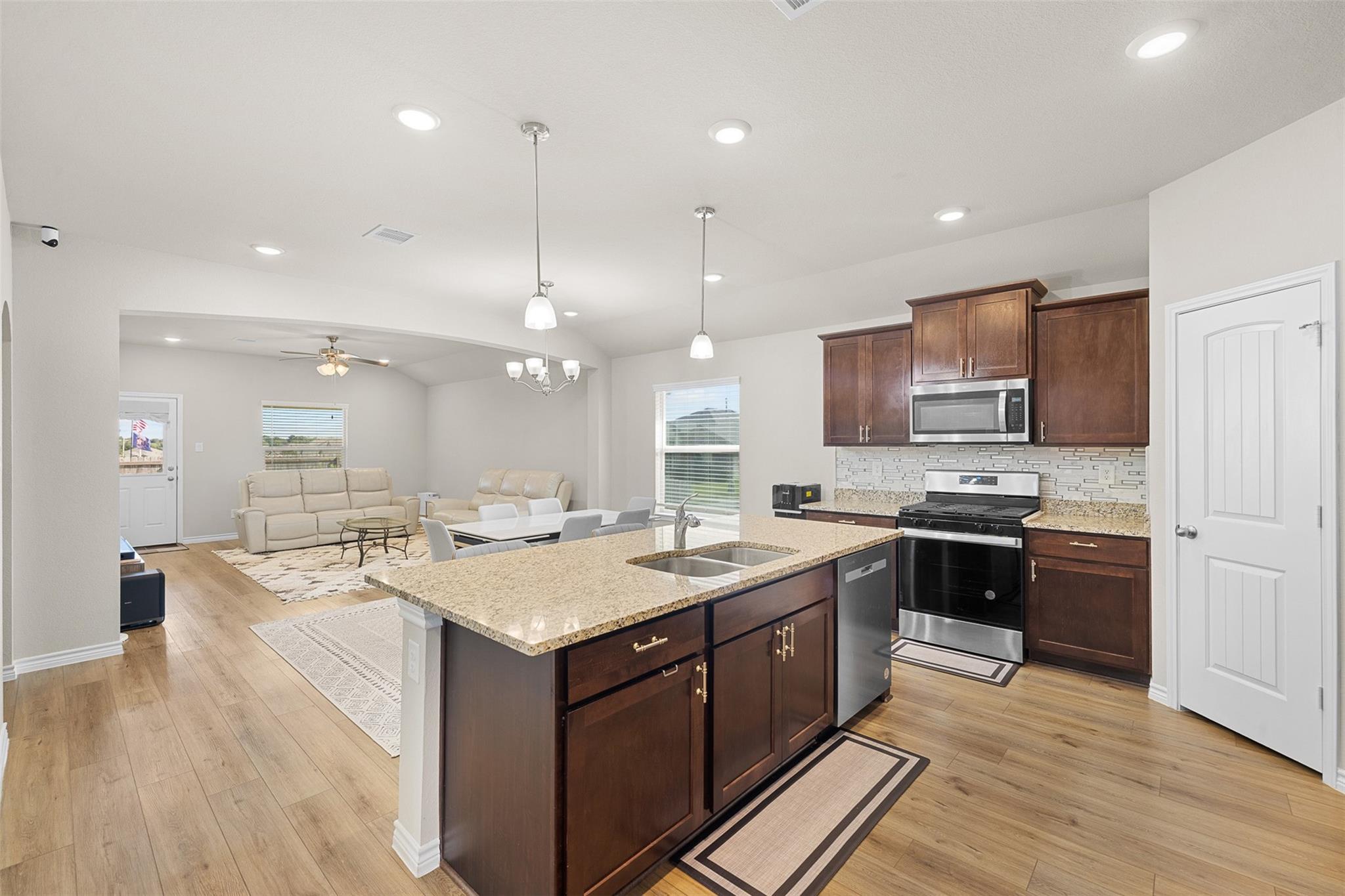 Open-plan kitchen with dark wood cabinets, granite island, stainless appliances, and adjoining furnished living area.