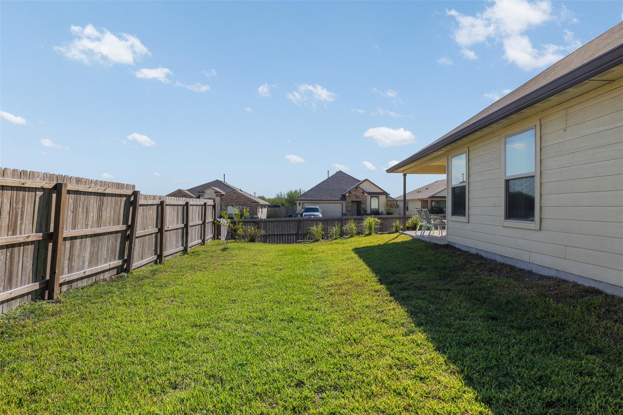 Grassy backyard beside the house, enclosed by a tall wooden fence with a covered patio at the far end.