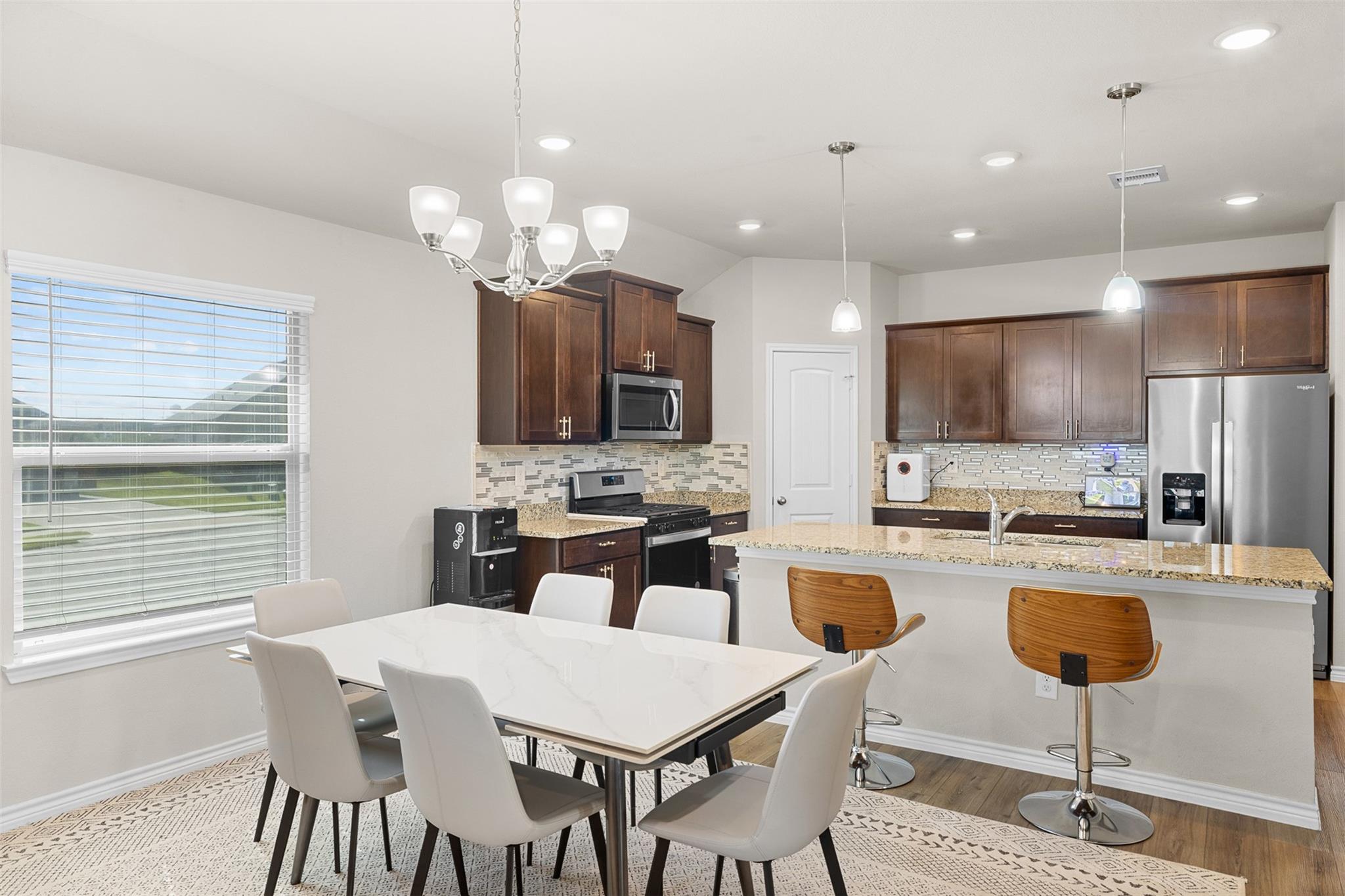 Kitchen with dark wood cabinets, stainless steel appliances, and a granite island beside a dining table.
