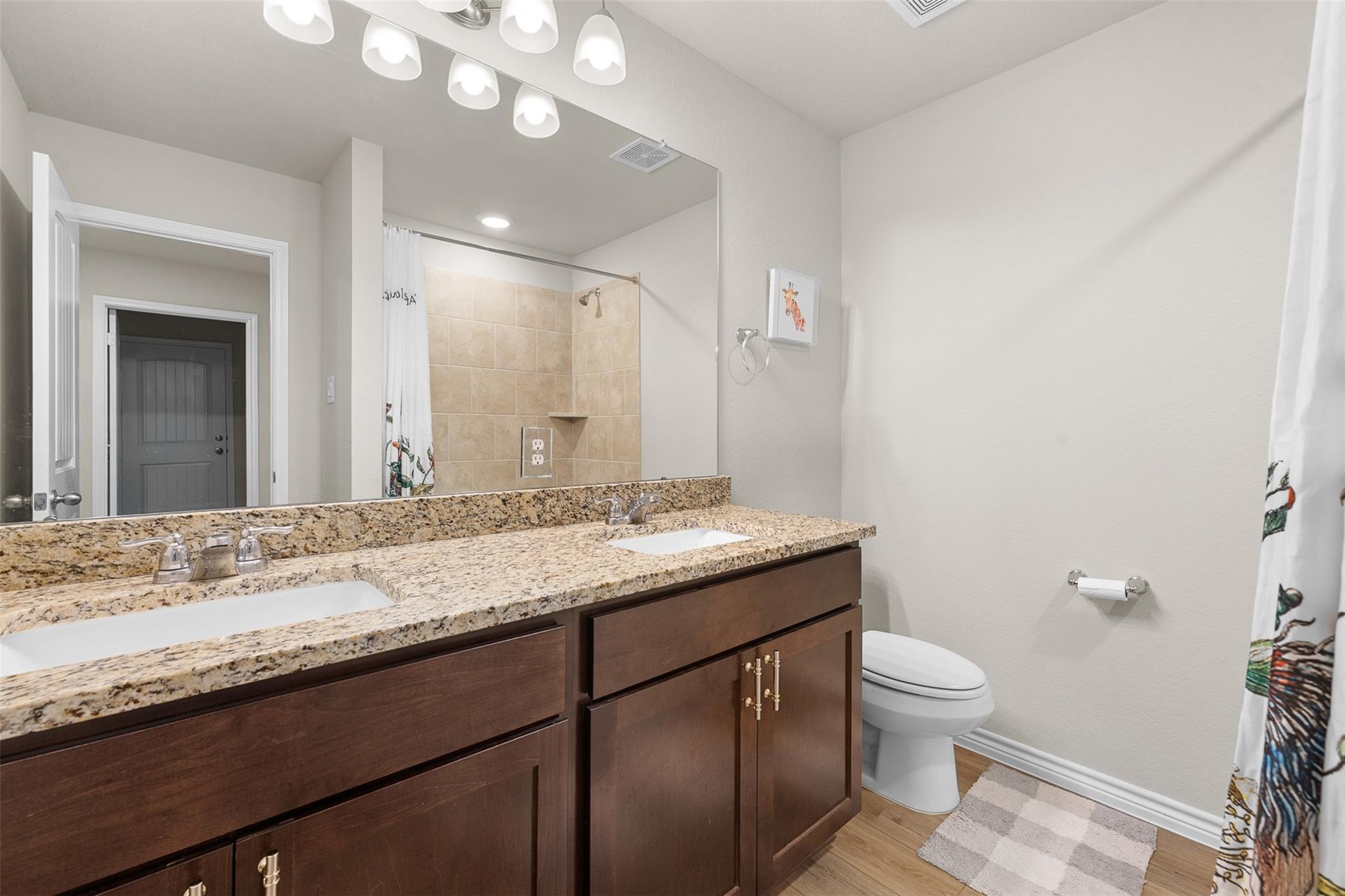 Bathroom with double-sink granite vanity, large mirror, tiled shower, and toilet.