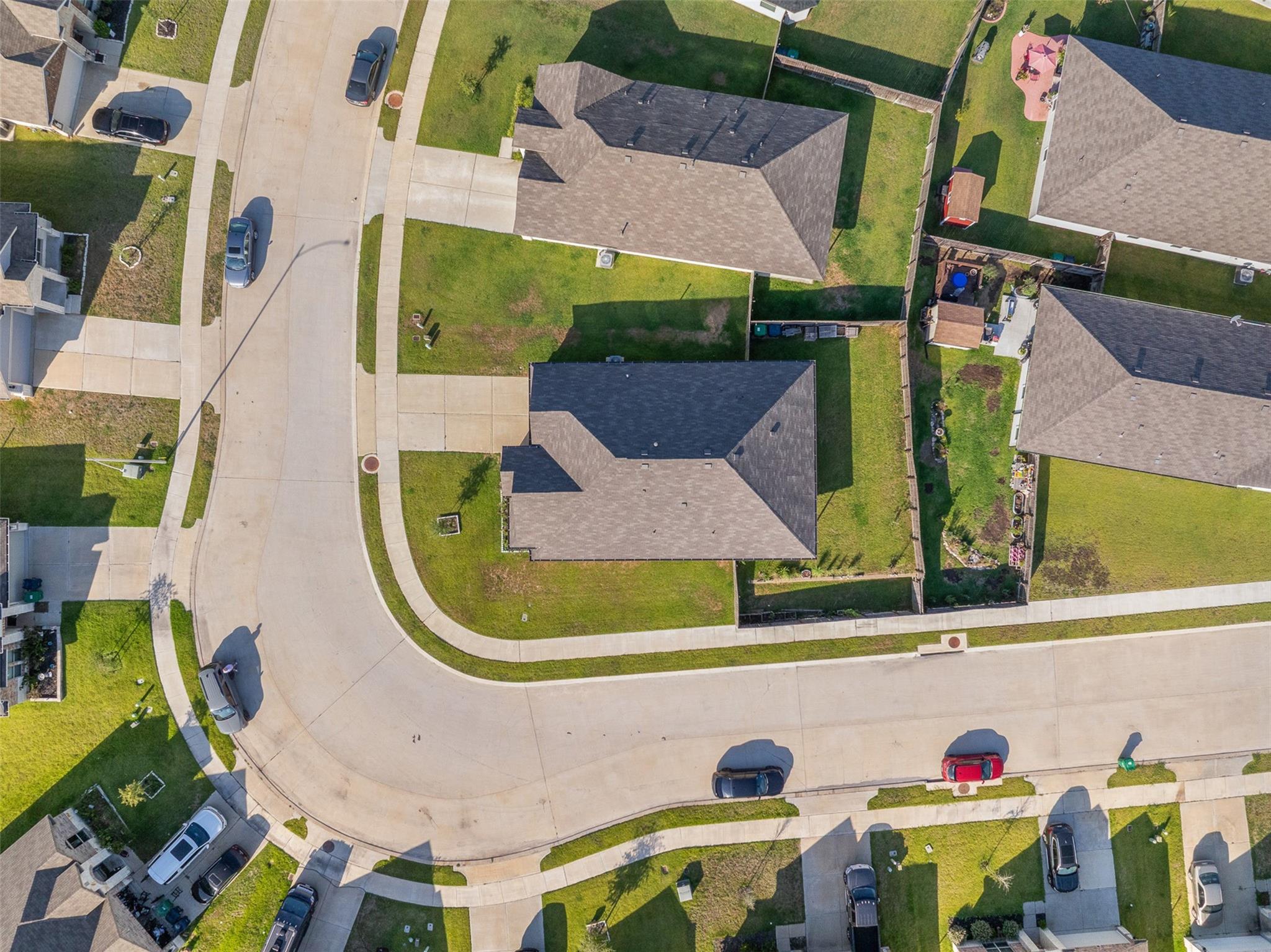 Aerial view of a house on a residential street, with a fenced lawn and neighboring homes.