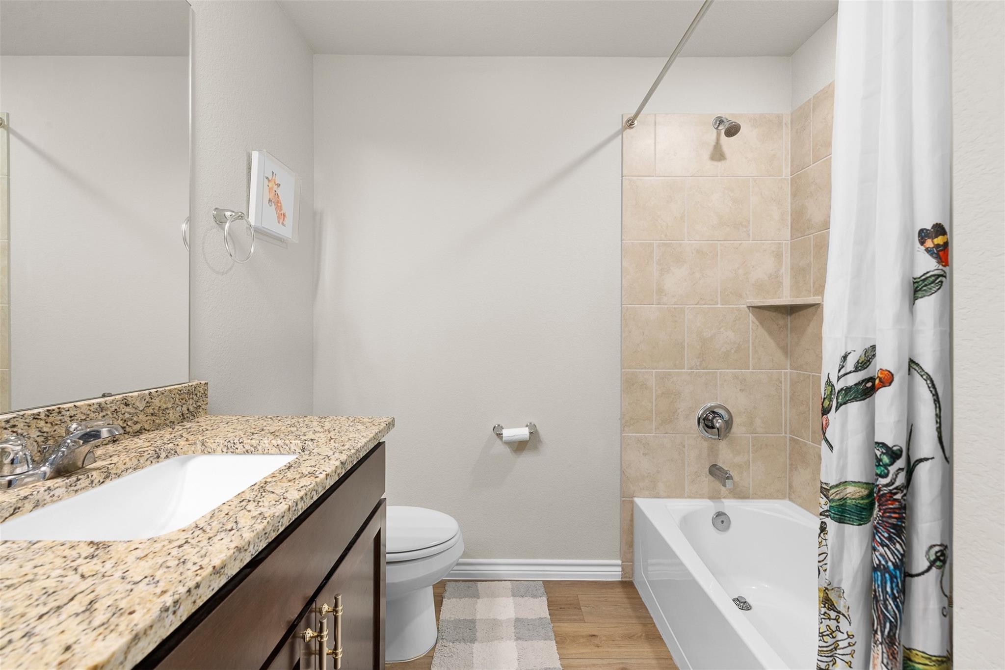 Bathroom with granite vanity, toilet, and beige-tiled bathtub surround.