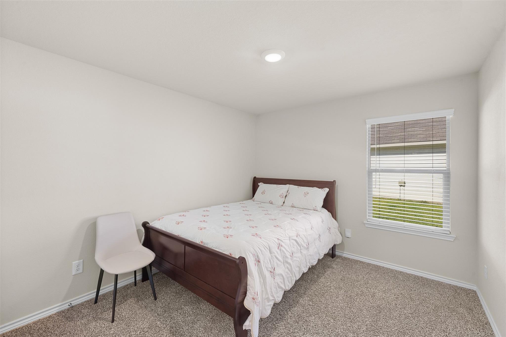 Furnished bedroom with a dark wood bed, white floral bedding, and a window with blinds.