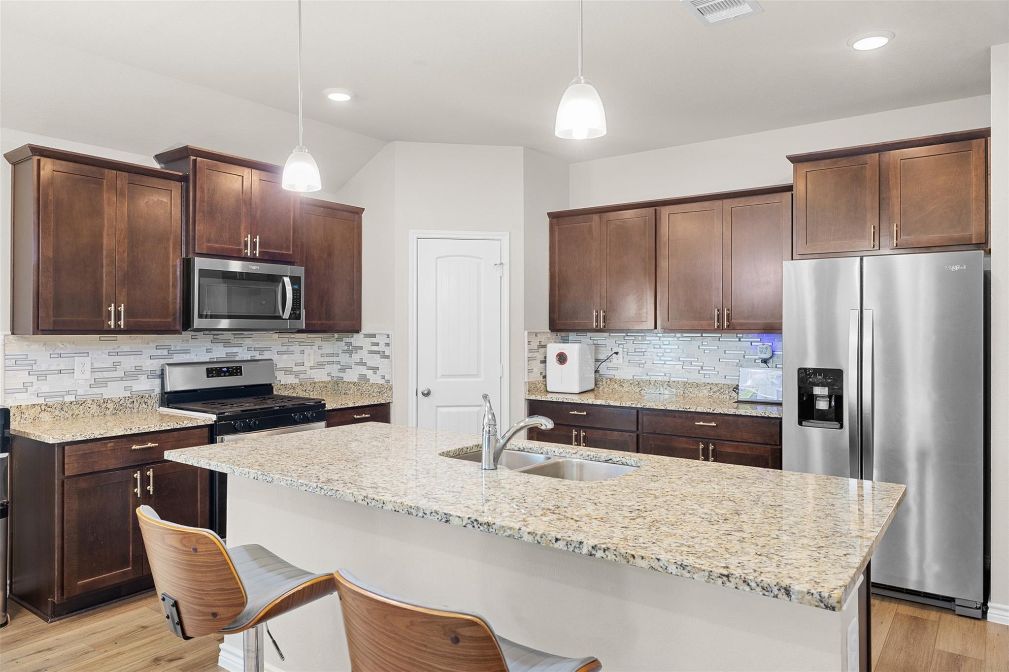 Kitchen with a granite island, dark wood cabinets, and stainless steel appliances.