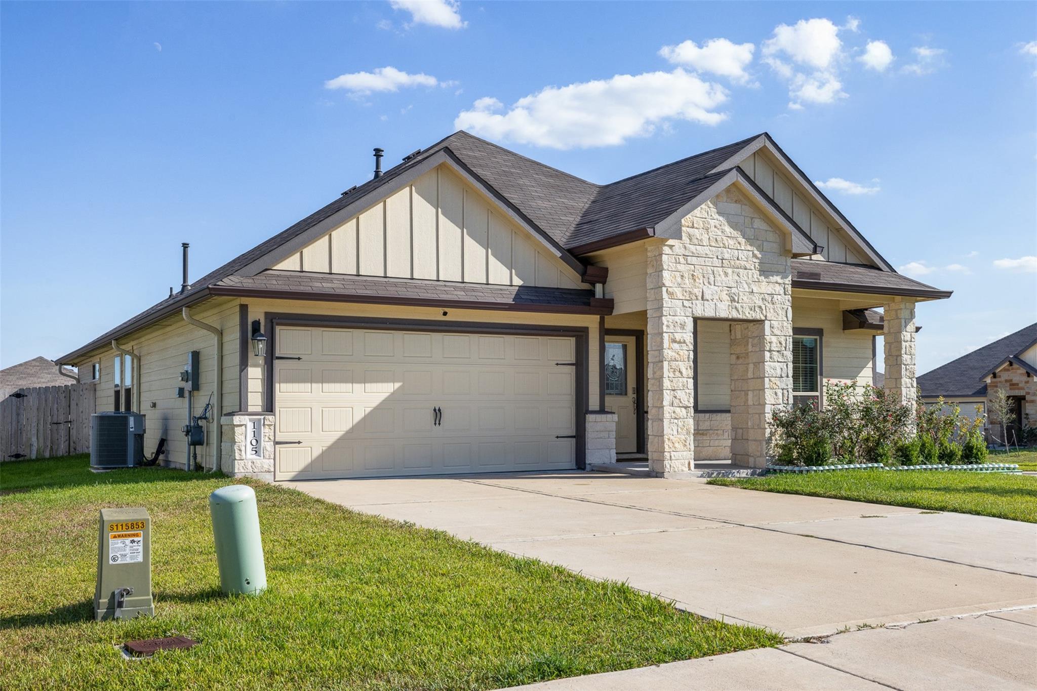 Cream-colored house with stone porch columns, a two-car garage, and a wide driveway.