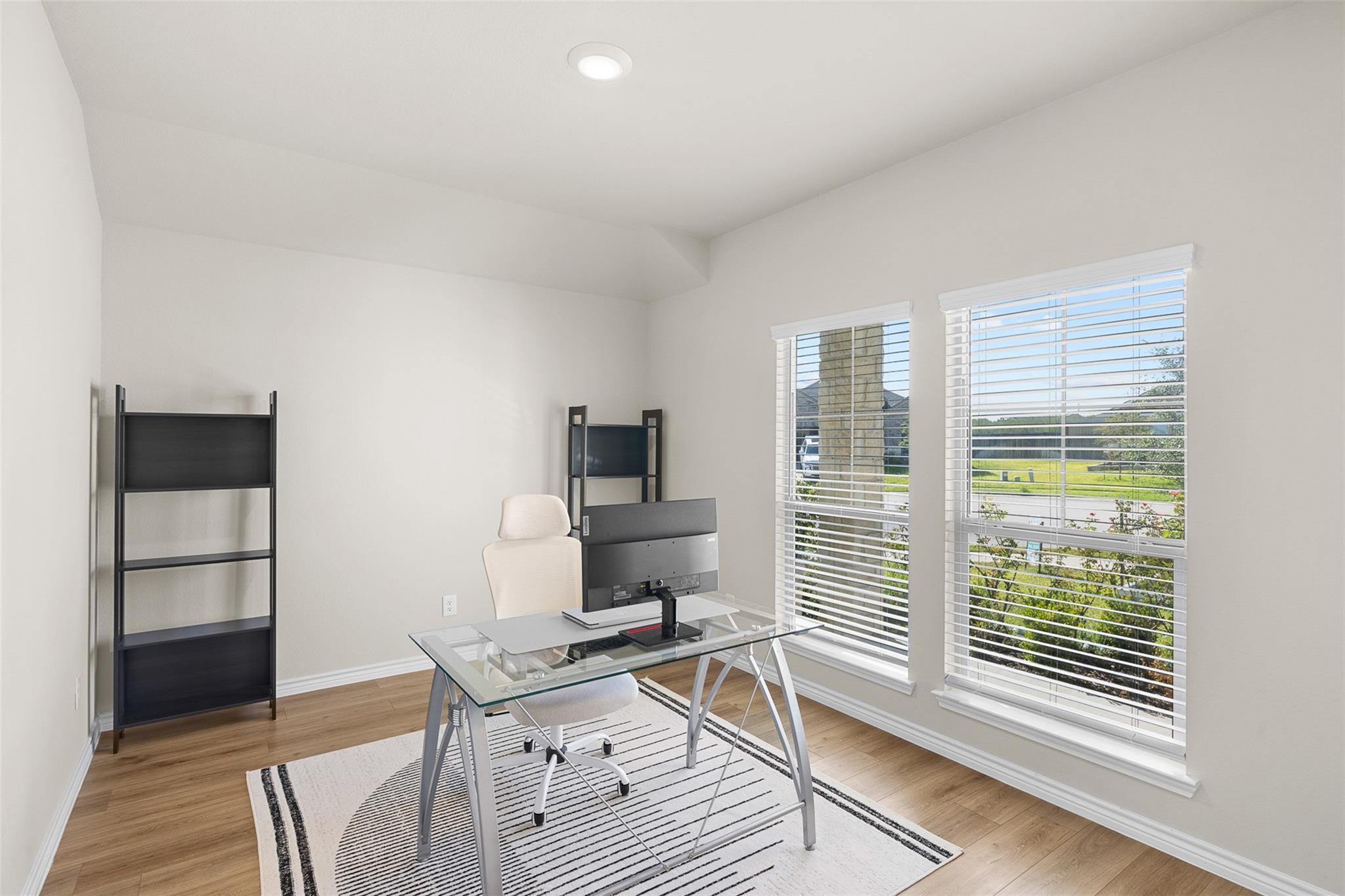 Home office with a glass desk and white chair beside two large windows.