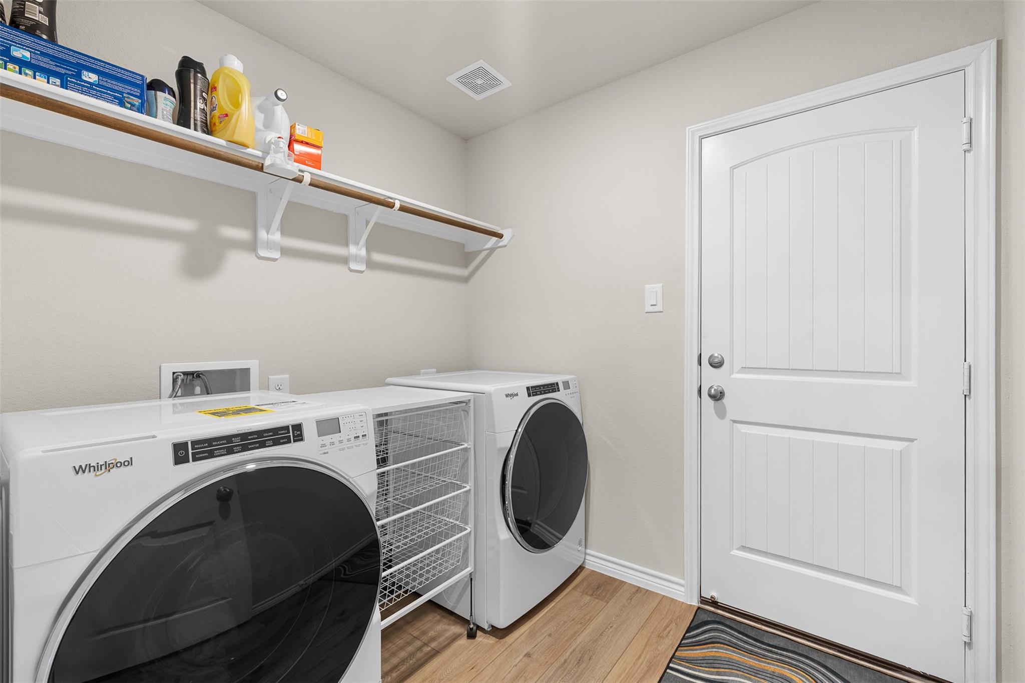 Laundry room with front-loading washer and dryer, wire storage cart, and a shelf of cleaning supplies.