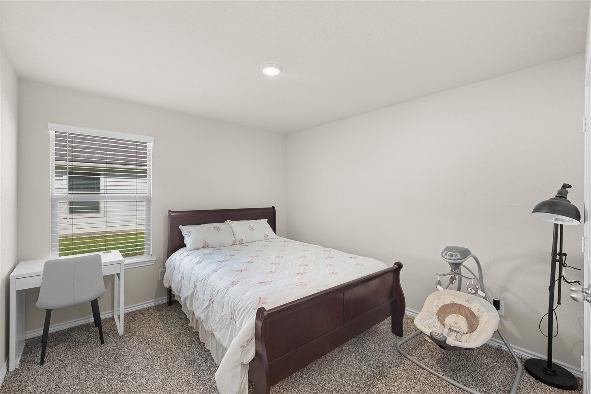 Bedroom with a dark wood bed, a desk by the window, and a baby swing.