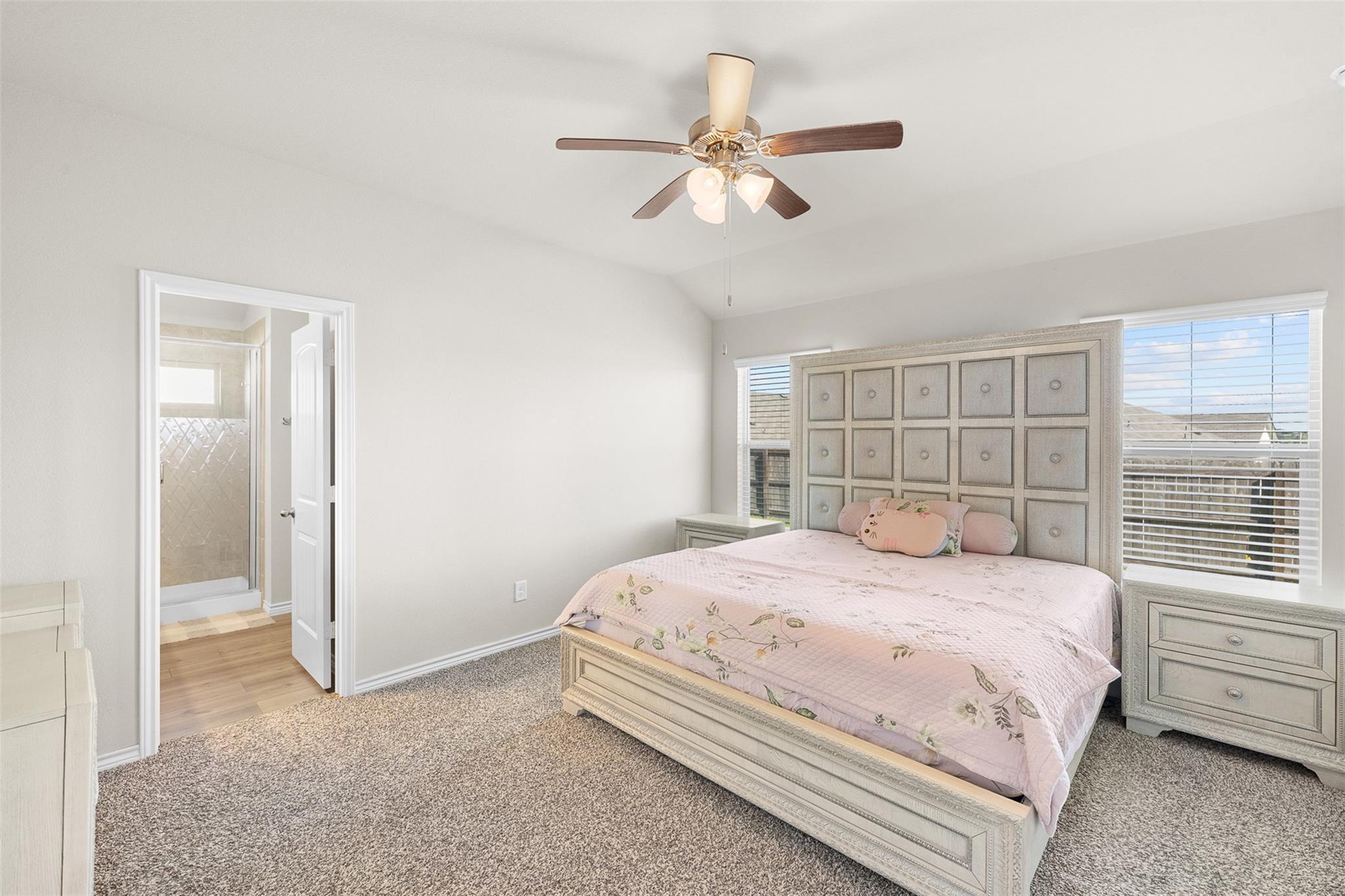 Bedroom with a pale pink floral quilt, ornate headboard, and open doorway to an ensuite bathroom.