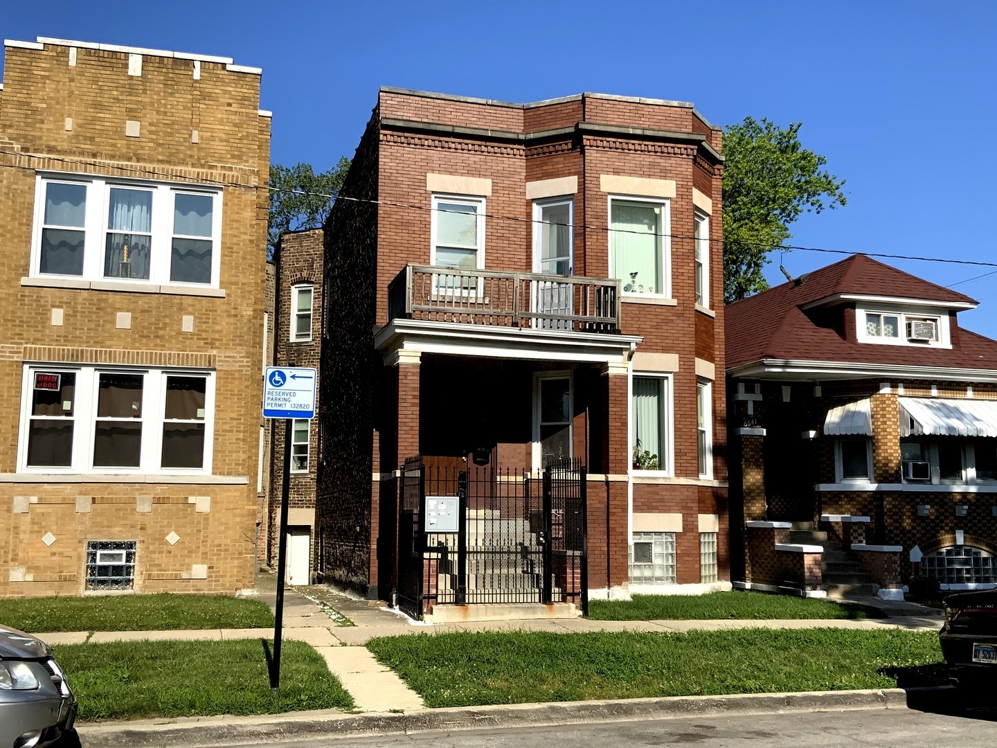 Two-story red brick Chicago home with an upper balcony and gated front entry.
