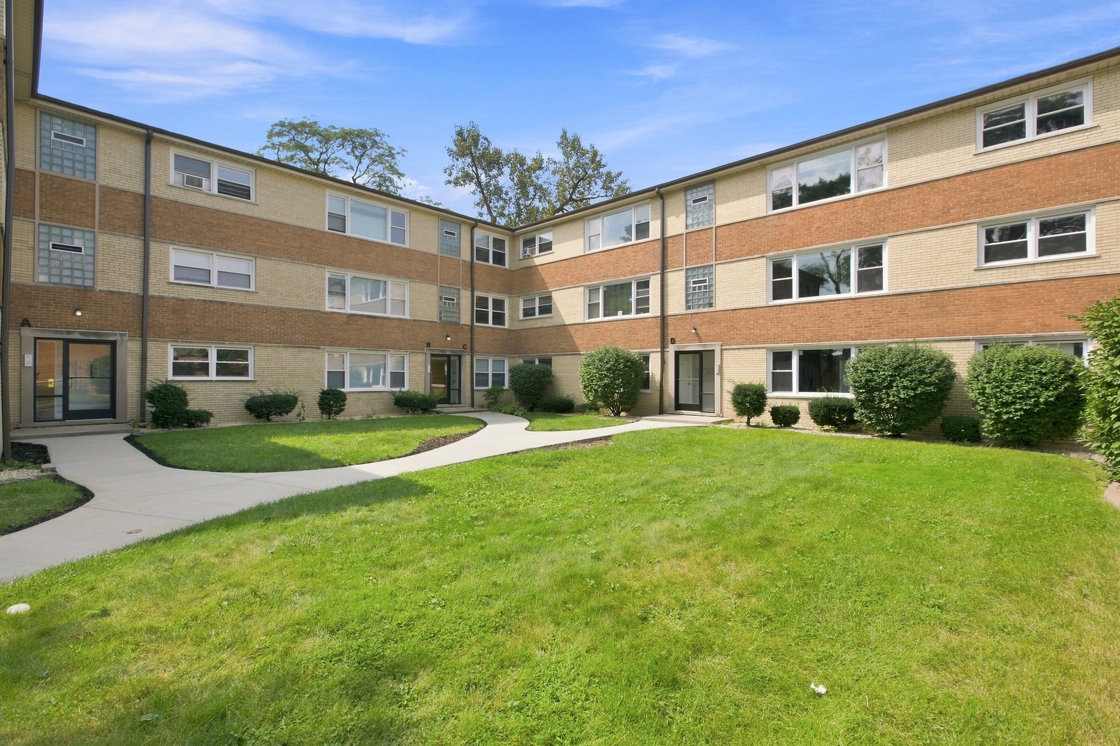 Three-story brick apartment building around a green courtyard with a curved walkway.