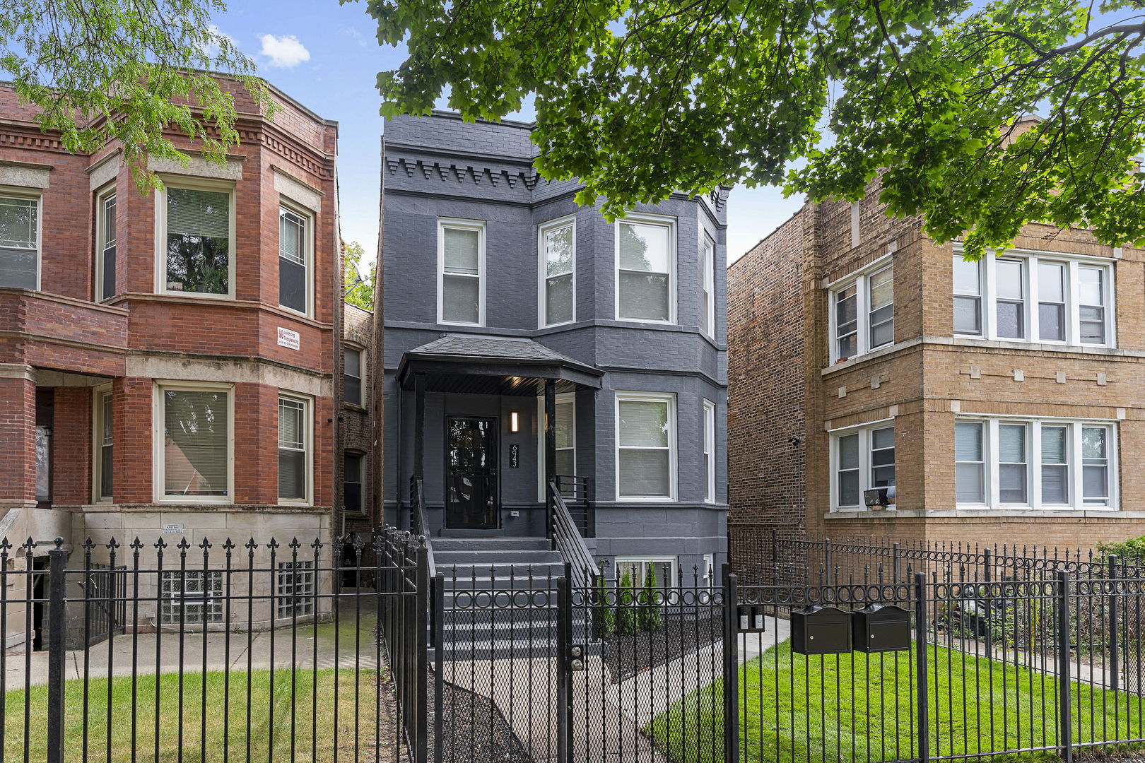 Gray brick Chicago building with a projecting bay, covered entrance, and black iron fence.
