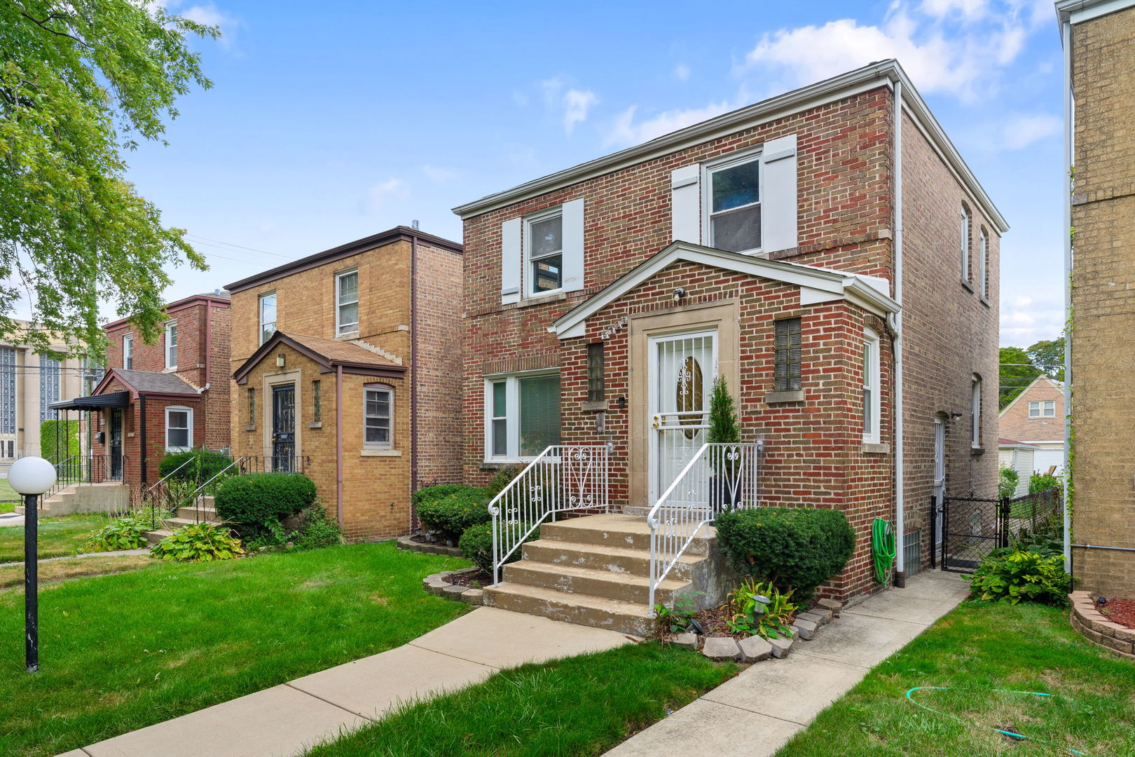 Two-story red brick house with a raised entry, white railings, and a green front lawn.