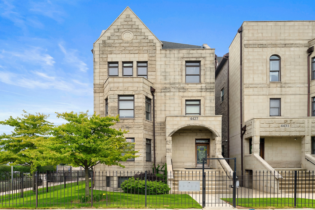 Stone Chicago home with a steep gable, arched entrance, and iron fence.