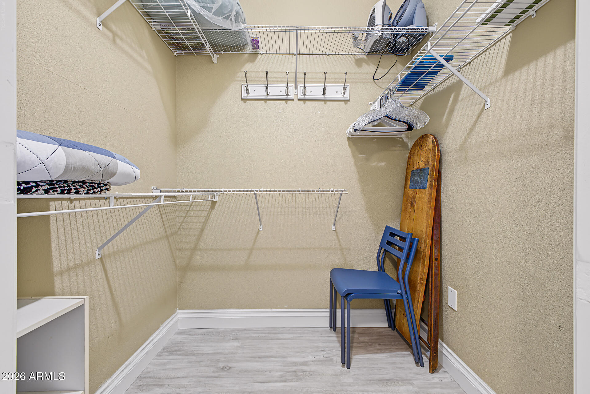 Walk-in closet with extensive wire shelving, hanging rails, bedding, and stored chairs.