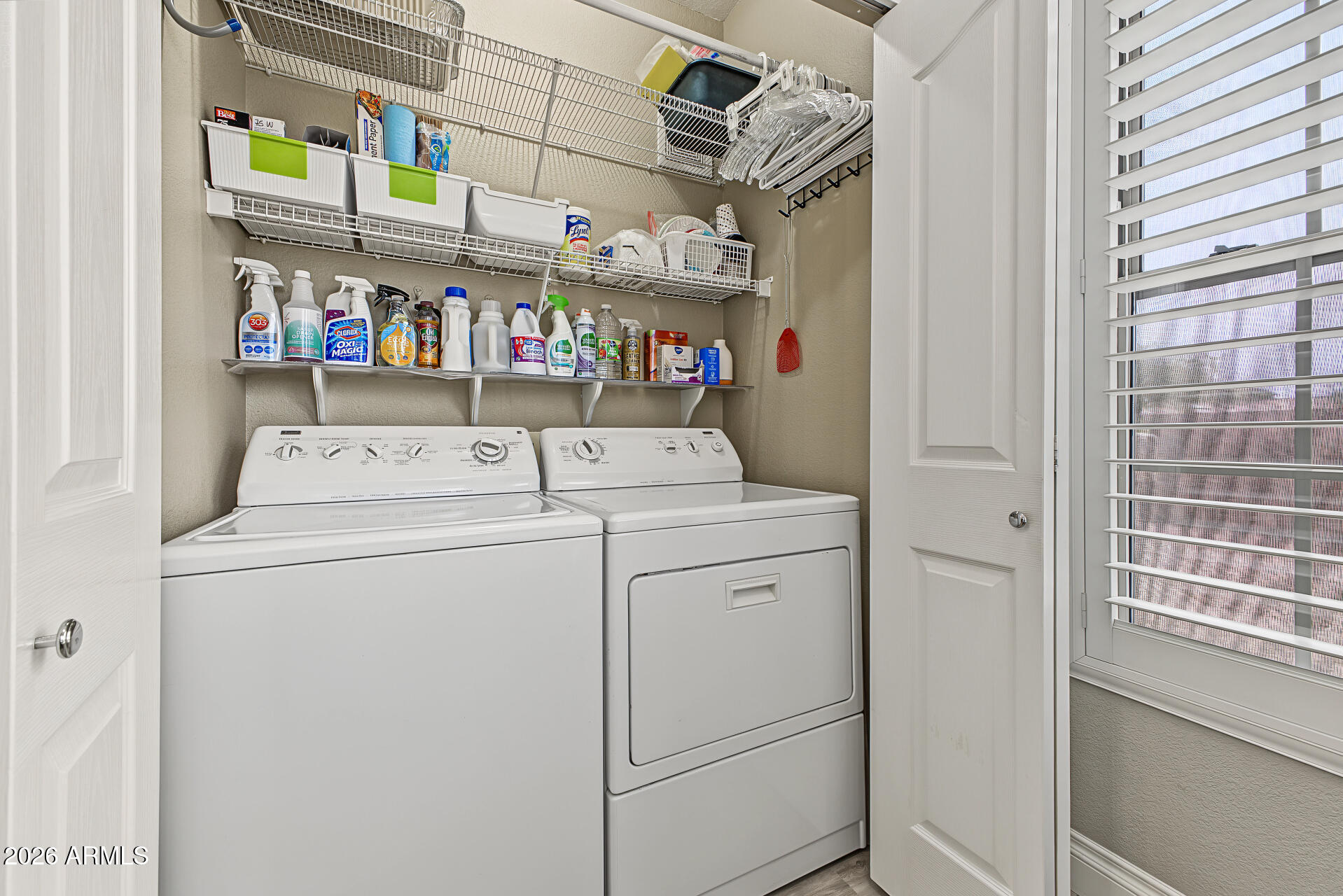 Laundry room with a washer and dryer beneath wire shelves stocked with cleaning supplies.