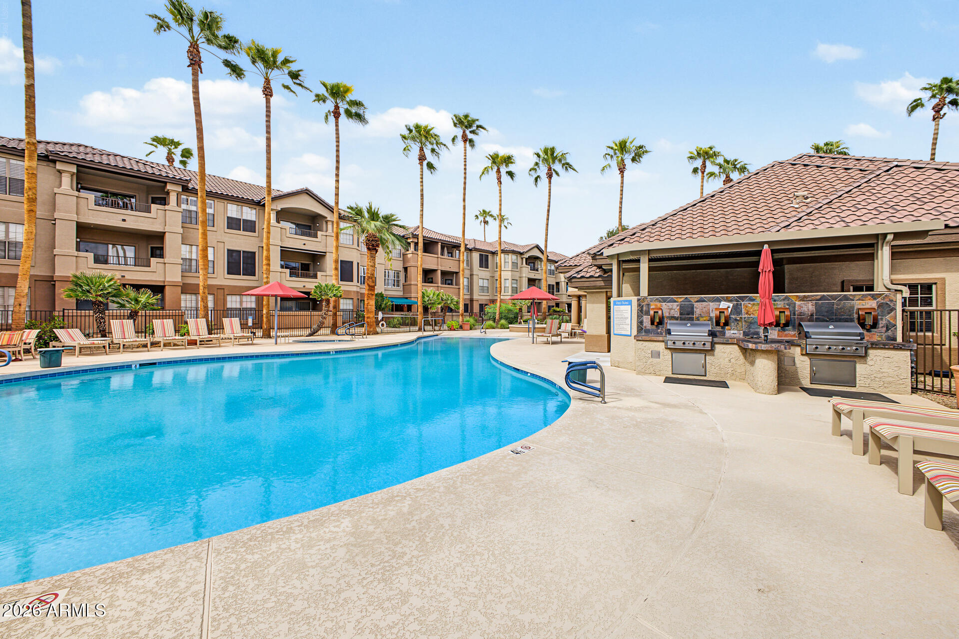 Community swimming pool beside apartment buildings, with palm trees and outdoor grills.