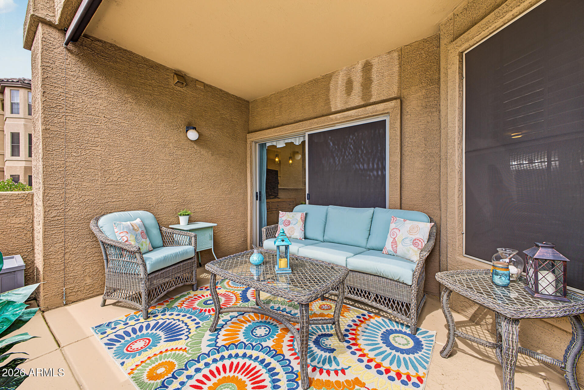 Covered patio with blue-cushioned wicker seating and a colorful floral rug.