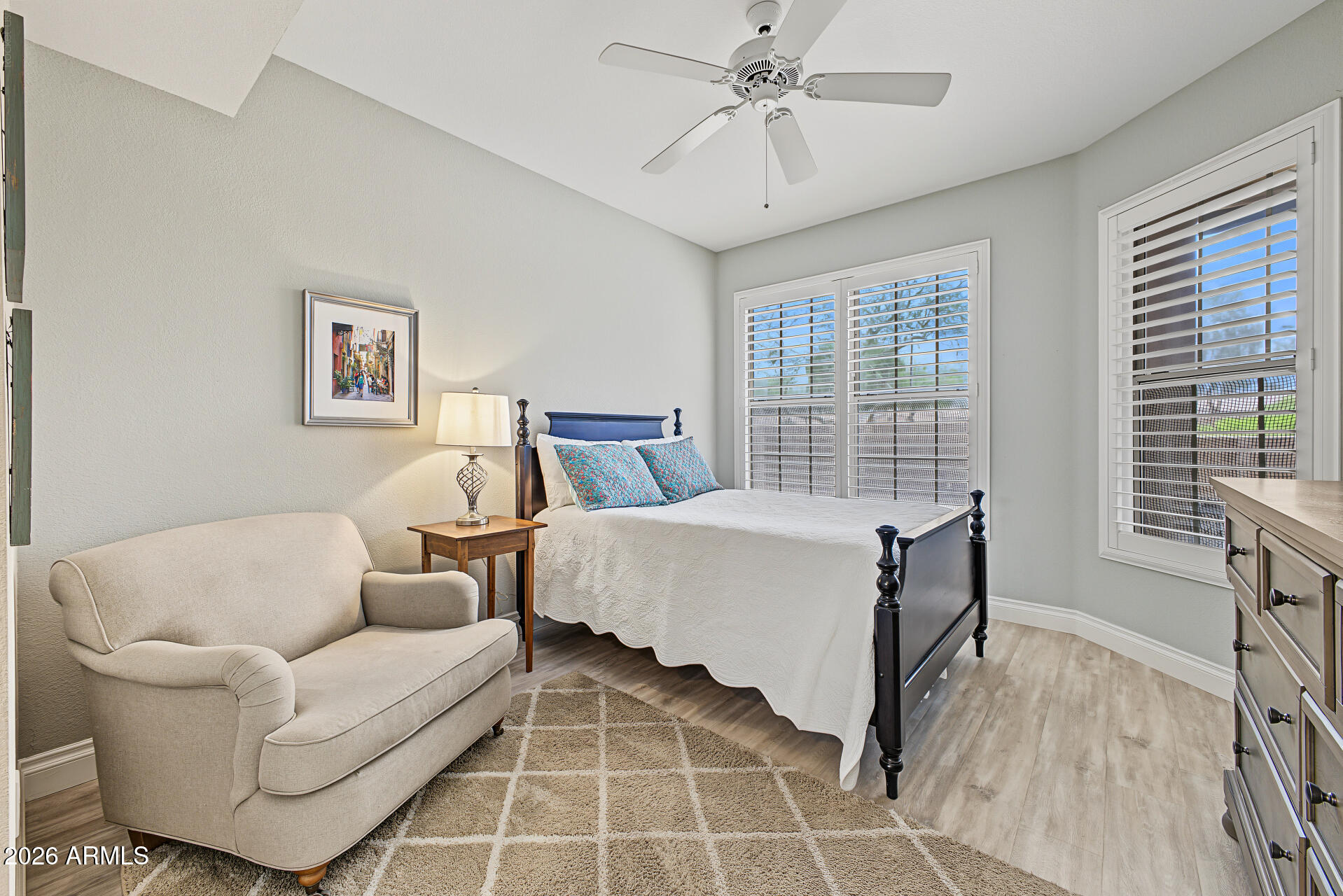 Bedroom with a dark wood bed, cream loveseat, and plantation-shuttered windows.