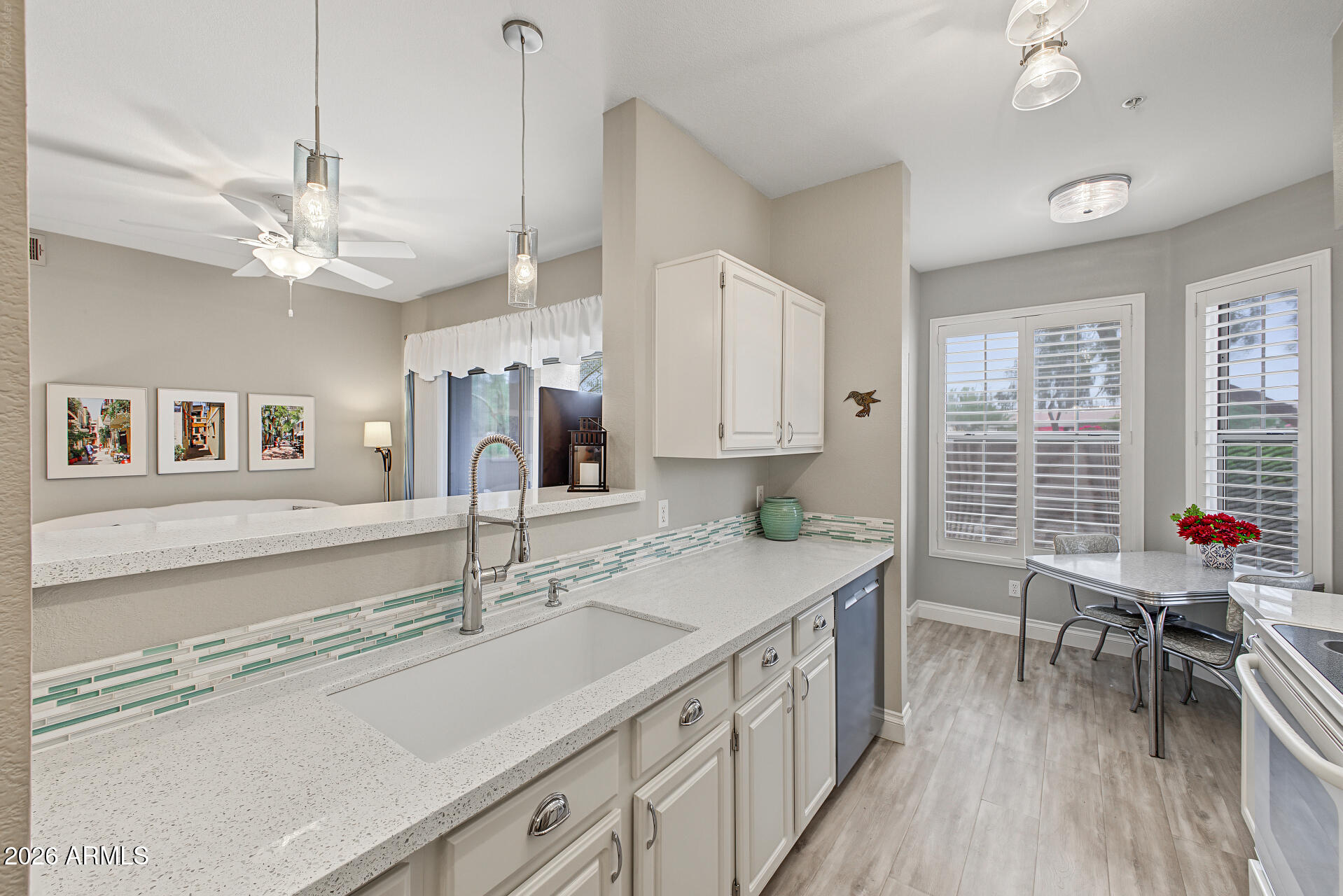 Kitchen with white cabinets, a green mosaic backsplash, and an adjoining dining area with shuttered windows.