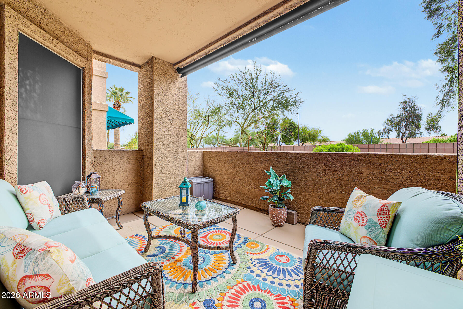 Covered patio with wicker seating, a glass-top table, and a colorful rug.