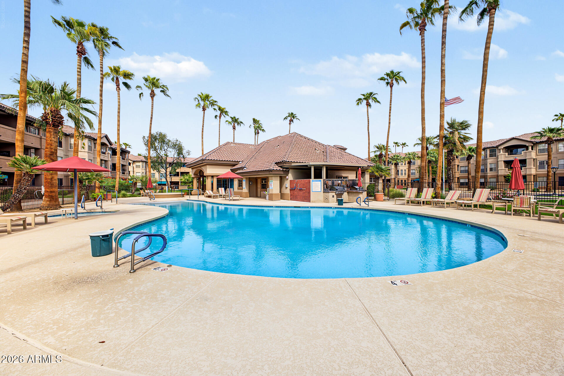 Apartment community pool with palm trees, lounge chairs, and a tiled-roof pavilion.