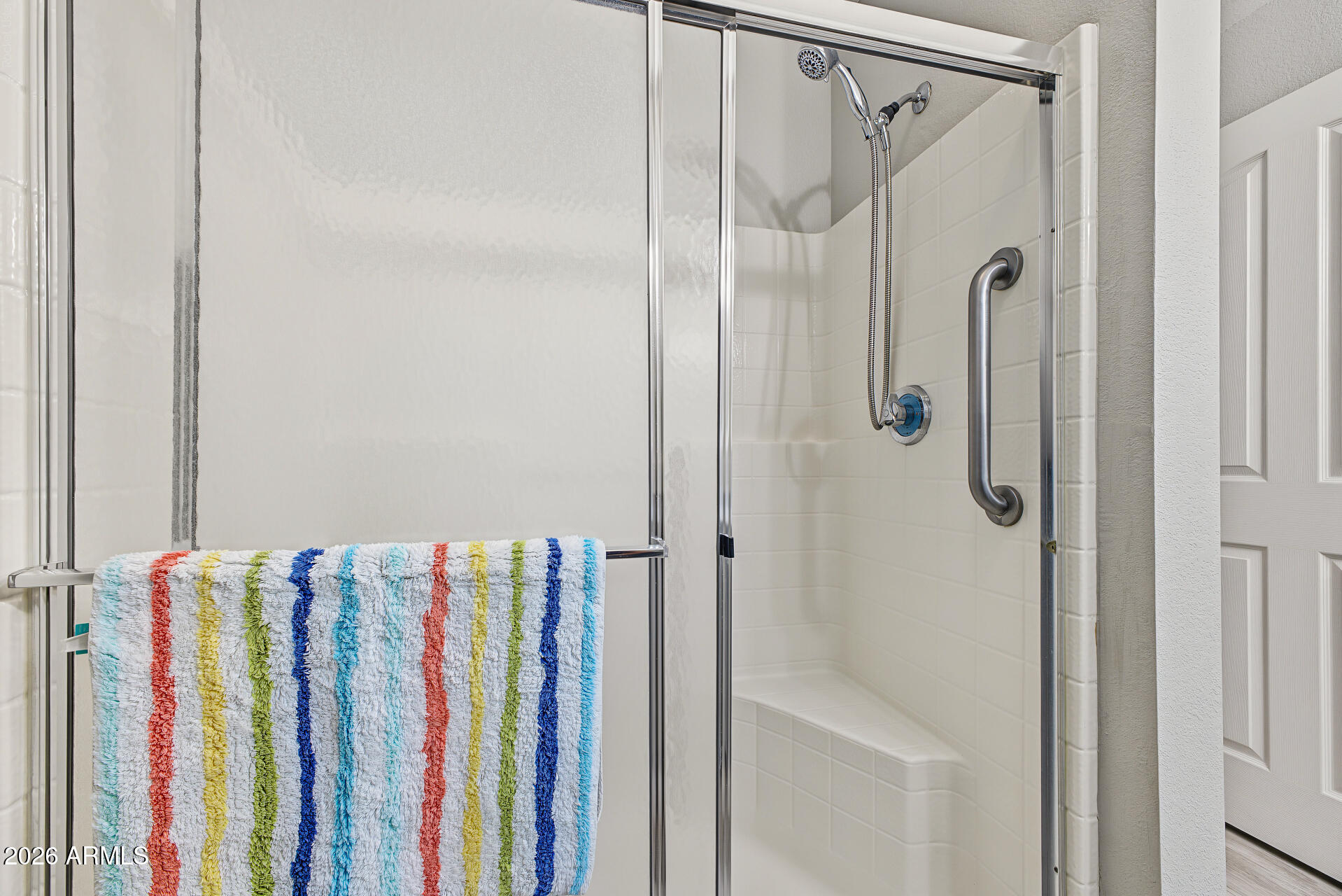White tiled walk-in shower with a glass enclosure, grab bar, and colorful striped towel.
