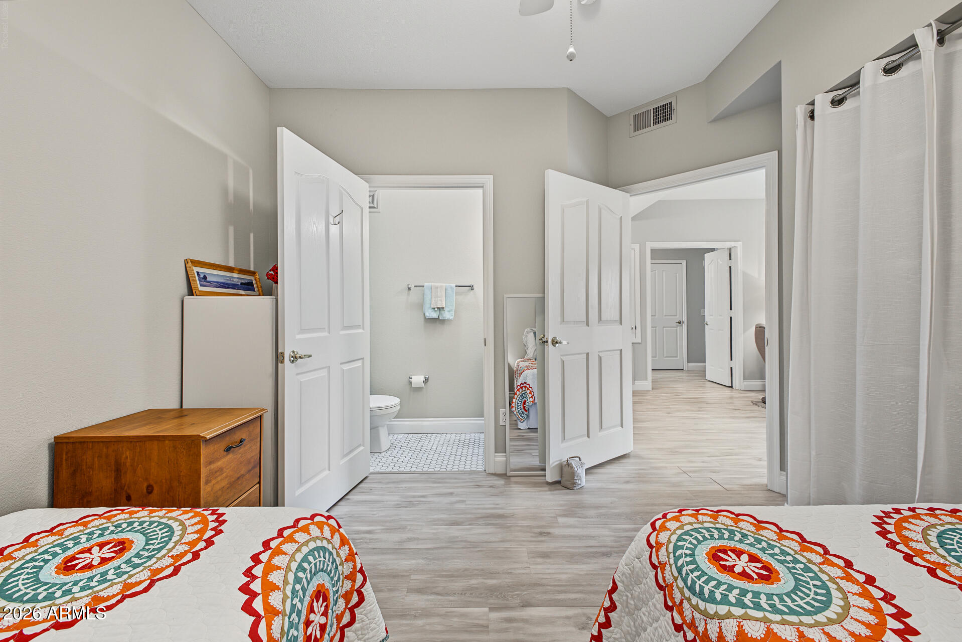 Furnished bedroom with colorful patterned quilts, opening to an ensuite bathroom and hallway.