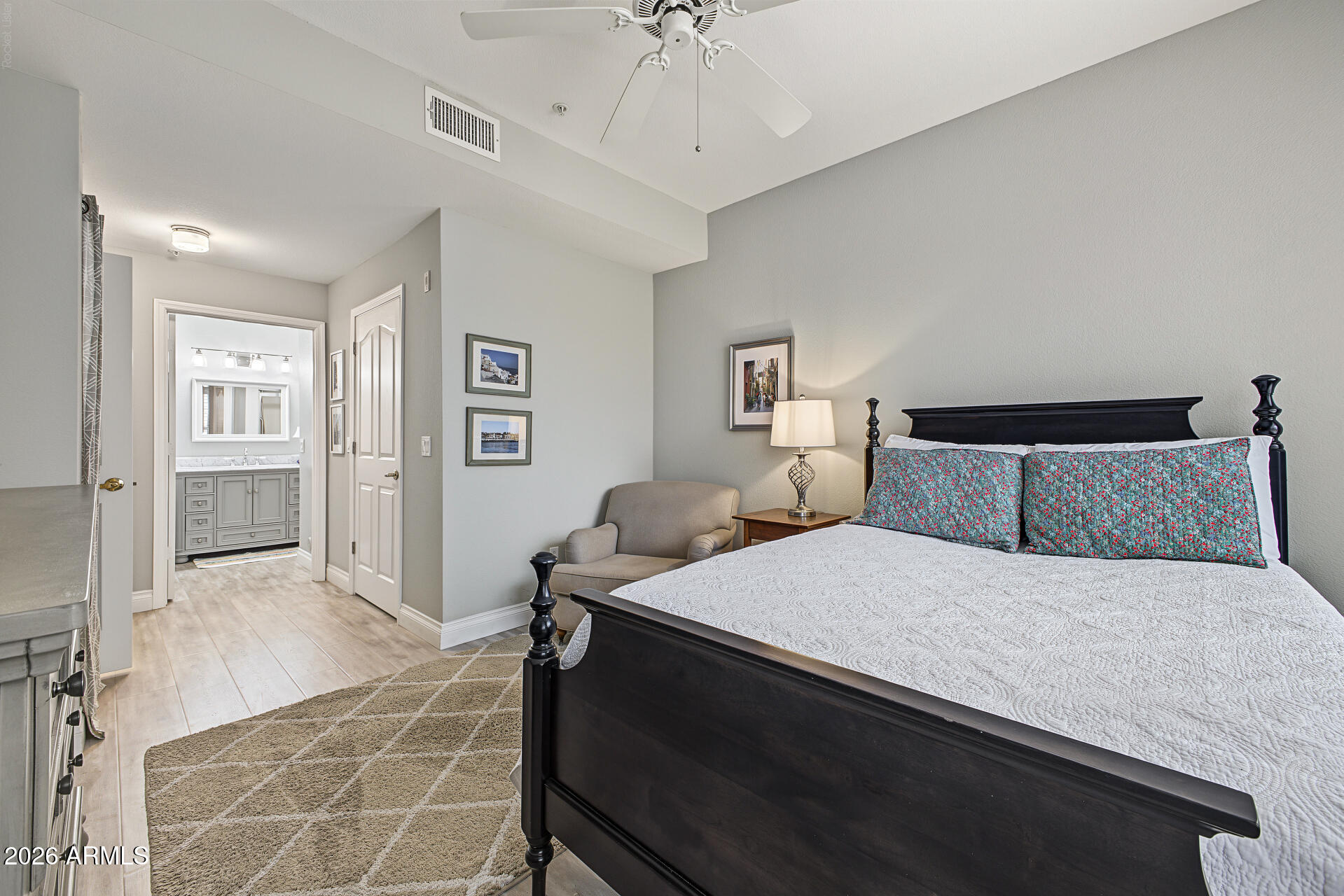 Bedroom with a dark wood bed and patterned turquoise pillows, opening to a bathroom with a double vanity.