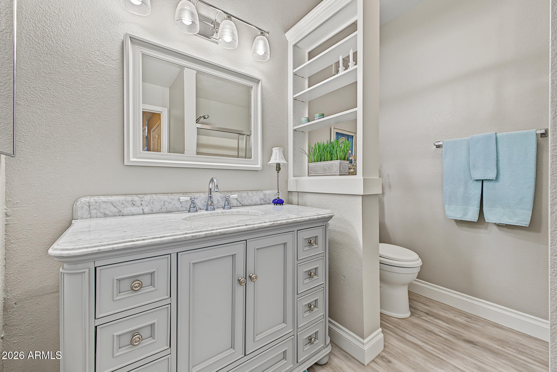Bathroom with a white paneled vanity, marble countertop, built-in shelves, and blue towels.