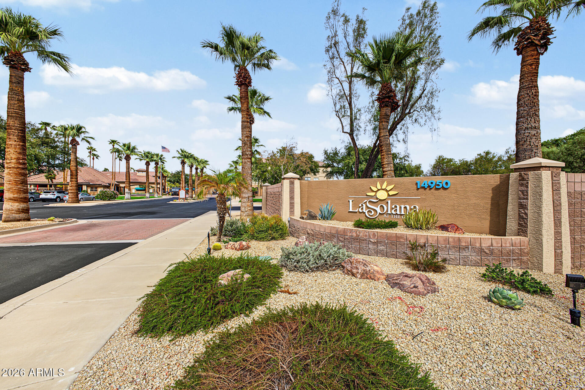 La Solana community entrance sign beside a palm-lined road and desert landscaping.