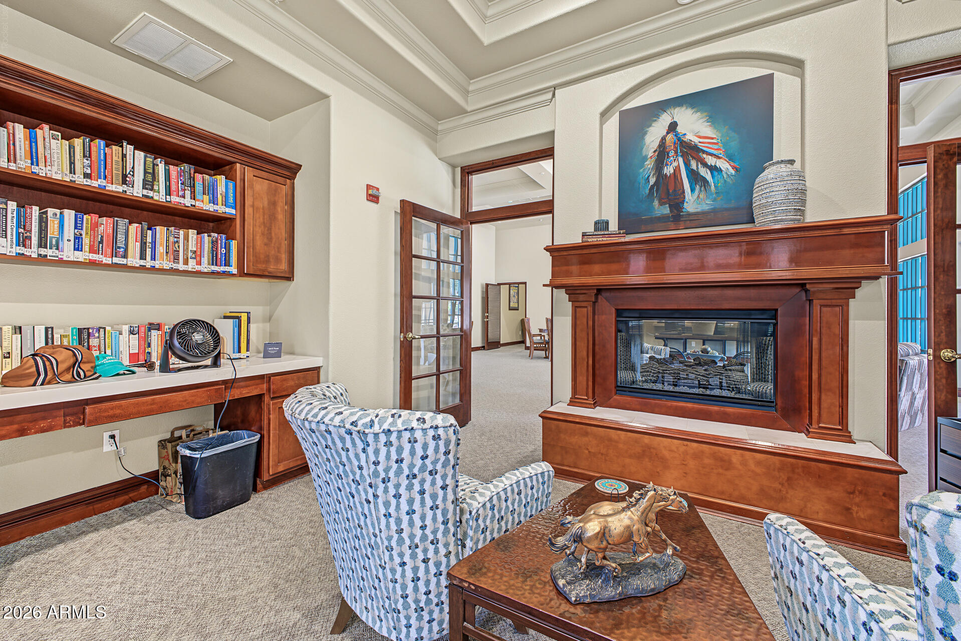 Furnished den with built-in bookshelves, patterned armchairs, and a large wood-trimmed fireplace.
