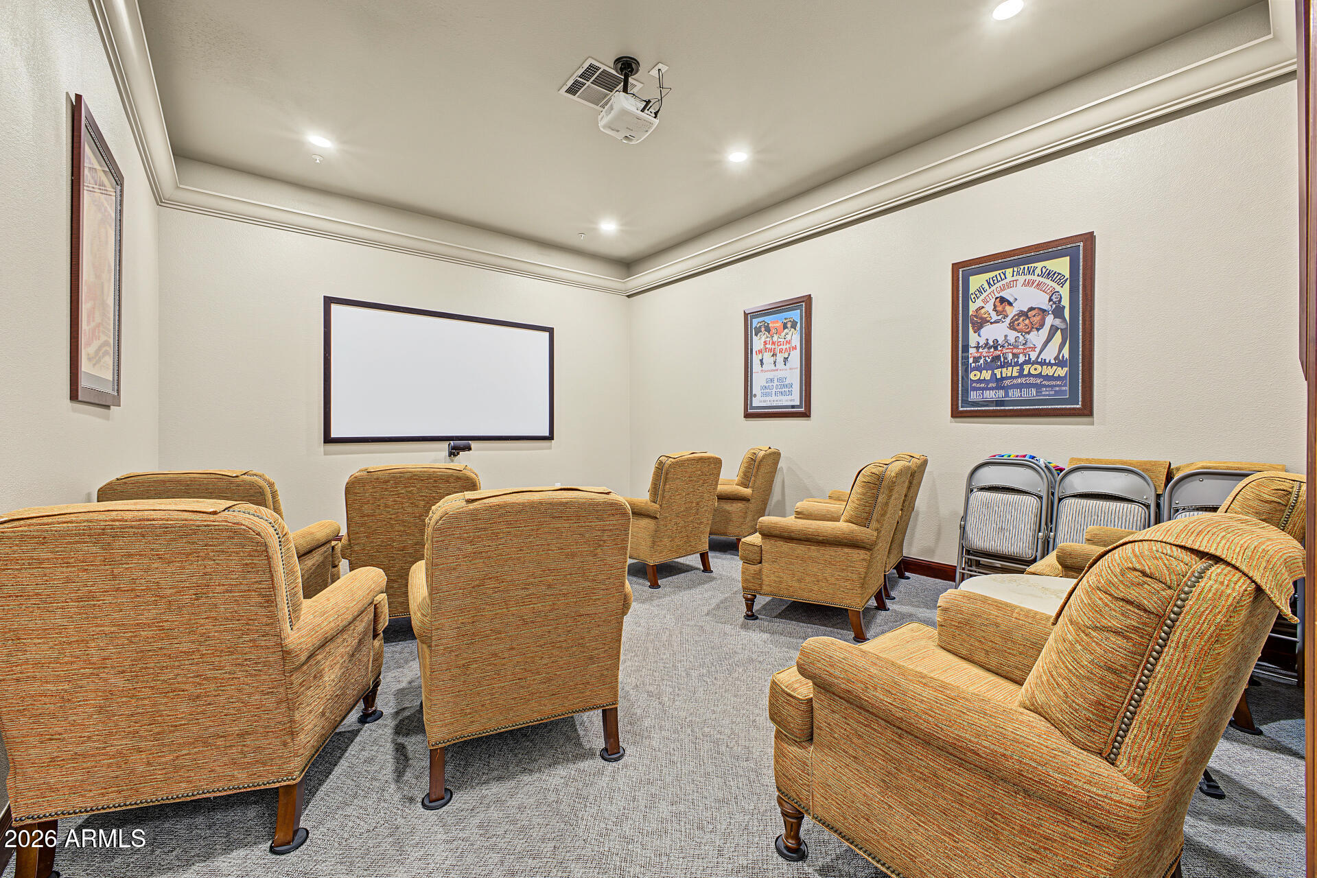 Home theater with upholstered armchairs, a large projection screen, ceiling-mounted projector, and framed movie posters.