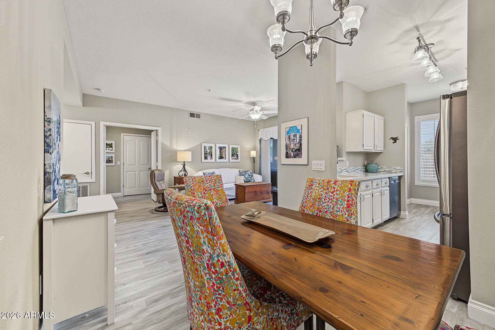 Open-plan condo dining area with a wooden table, colorful chairs, adjoining living room, and compact kitchen.