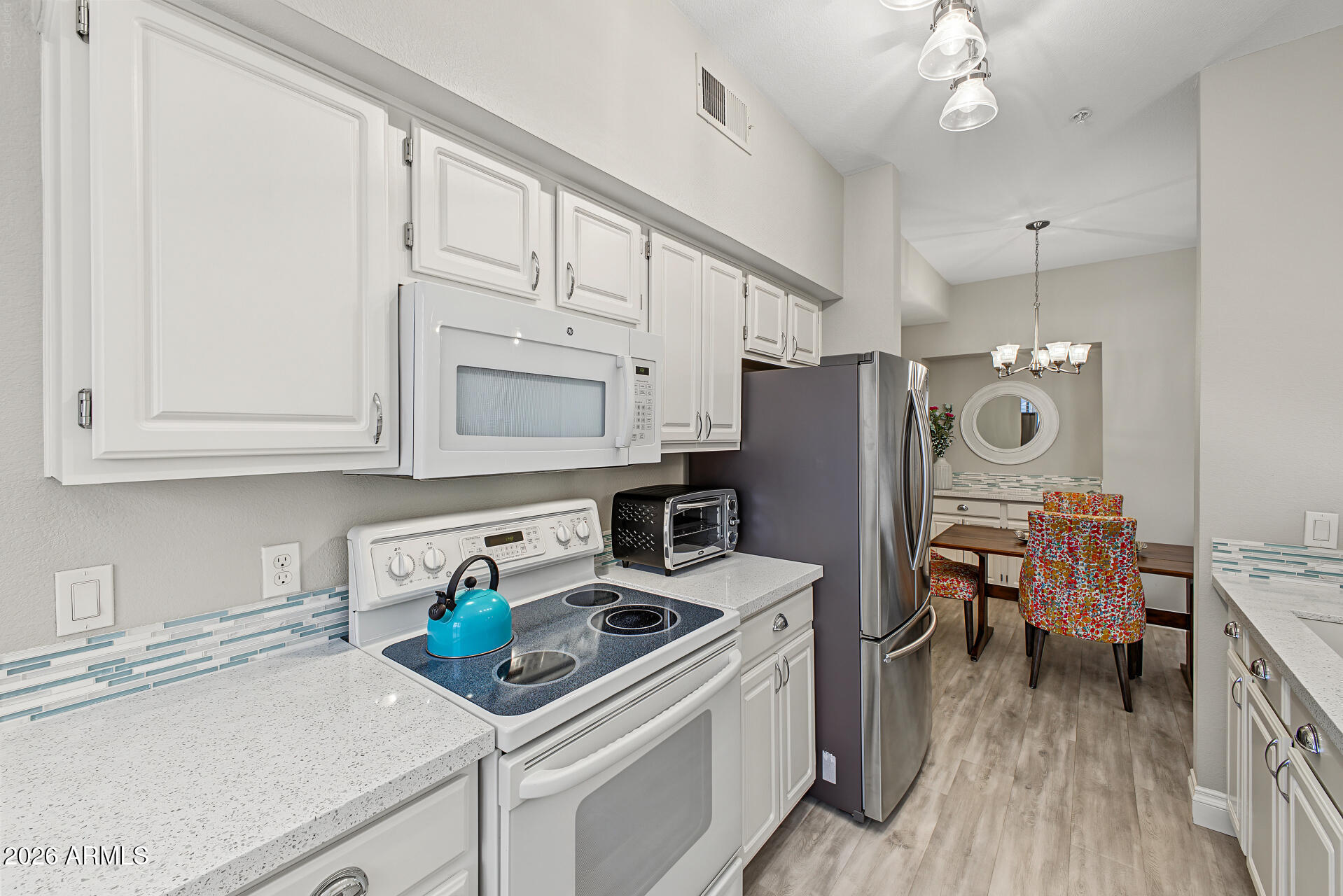 Kitchen with white cabinetry, blue tile backsplash, and a dining area with colorful chairs.