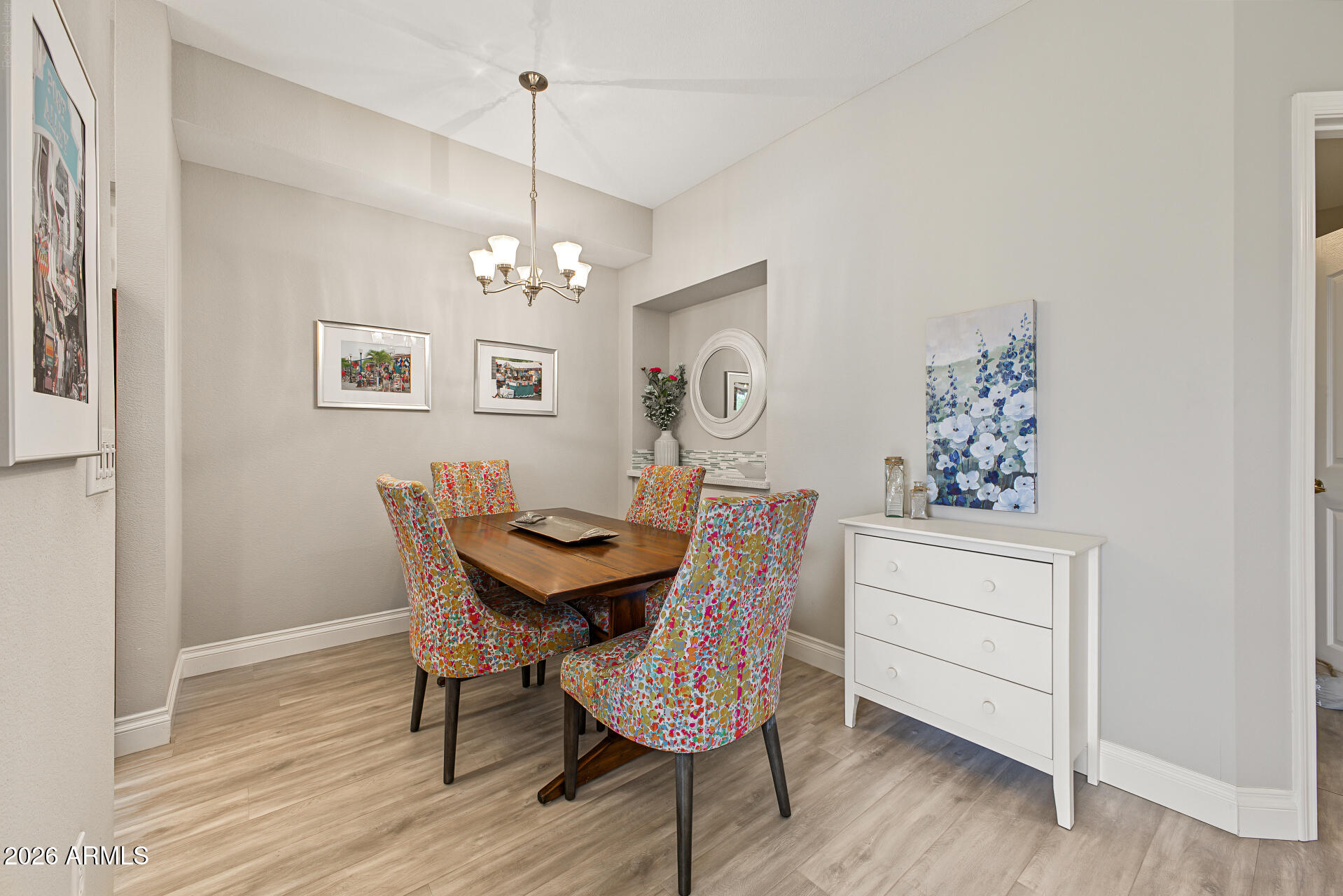 Dining room with a dark wood table, colorful chairs, chandelier, and white chest of drawers.