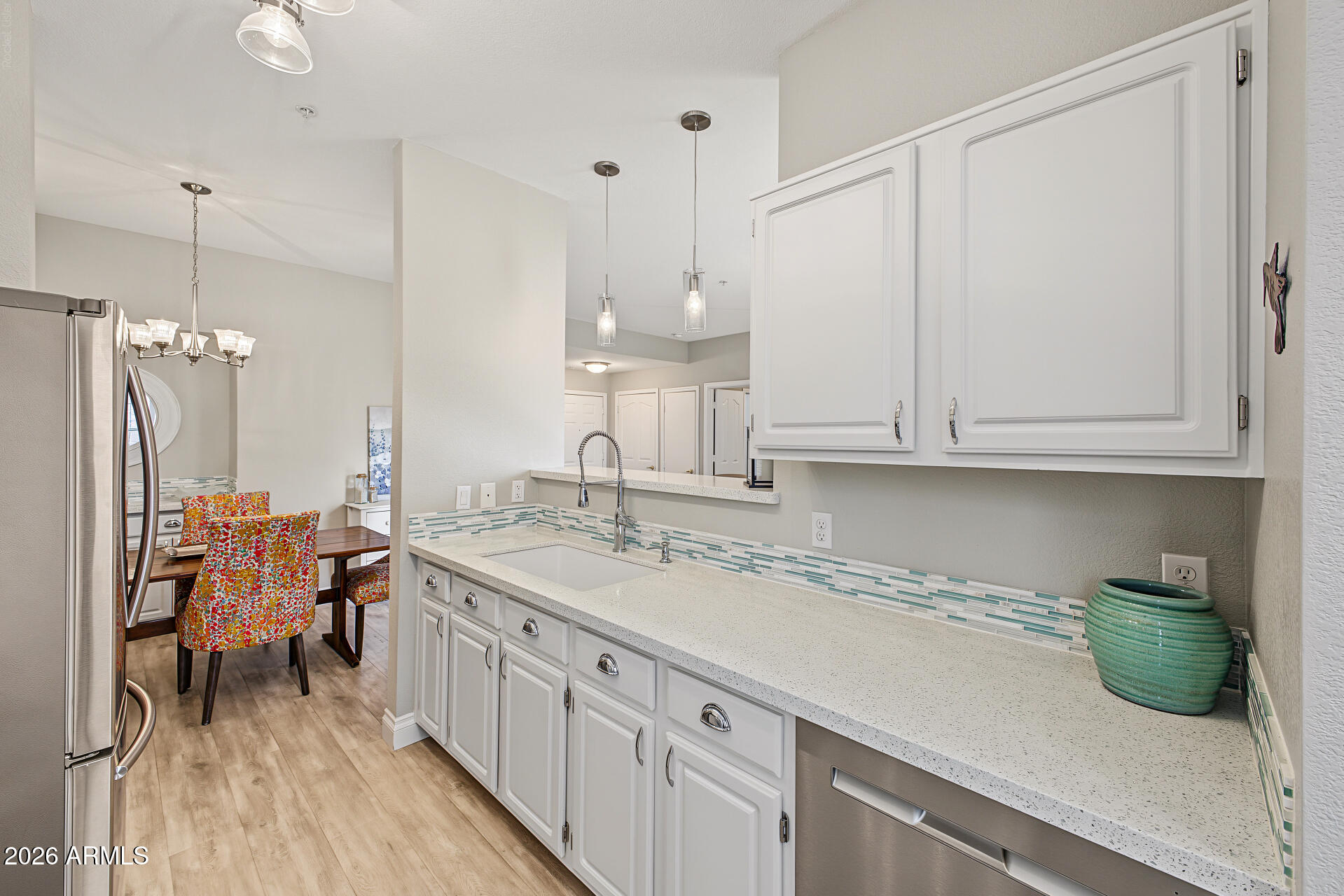 Kitchen with white cabinets, turquoise tile backsplash, and a dining area with colorful chairs.