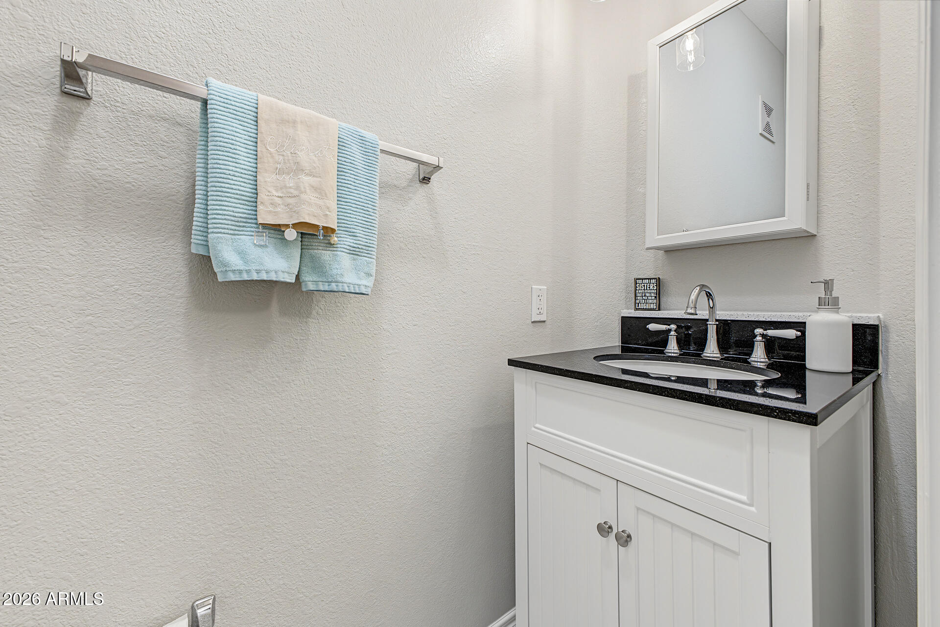 Bathroom vanity with black countertop, chrome faucet, framed mirror, and aqua towels.