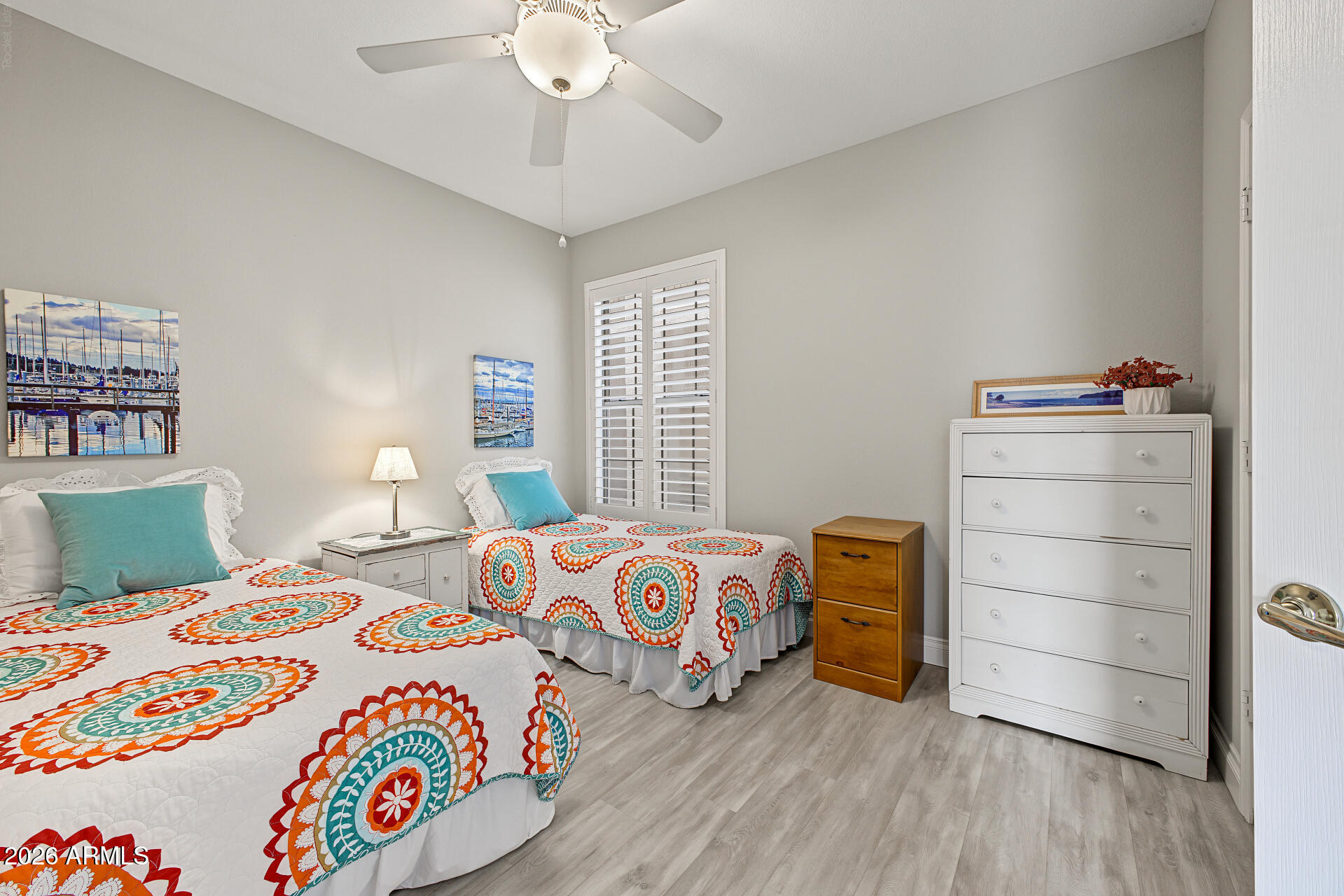 Bedroom with two twin beds in colorful medallion-patterned quilts and white plantation shutters.