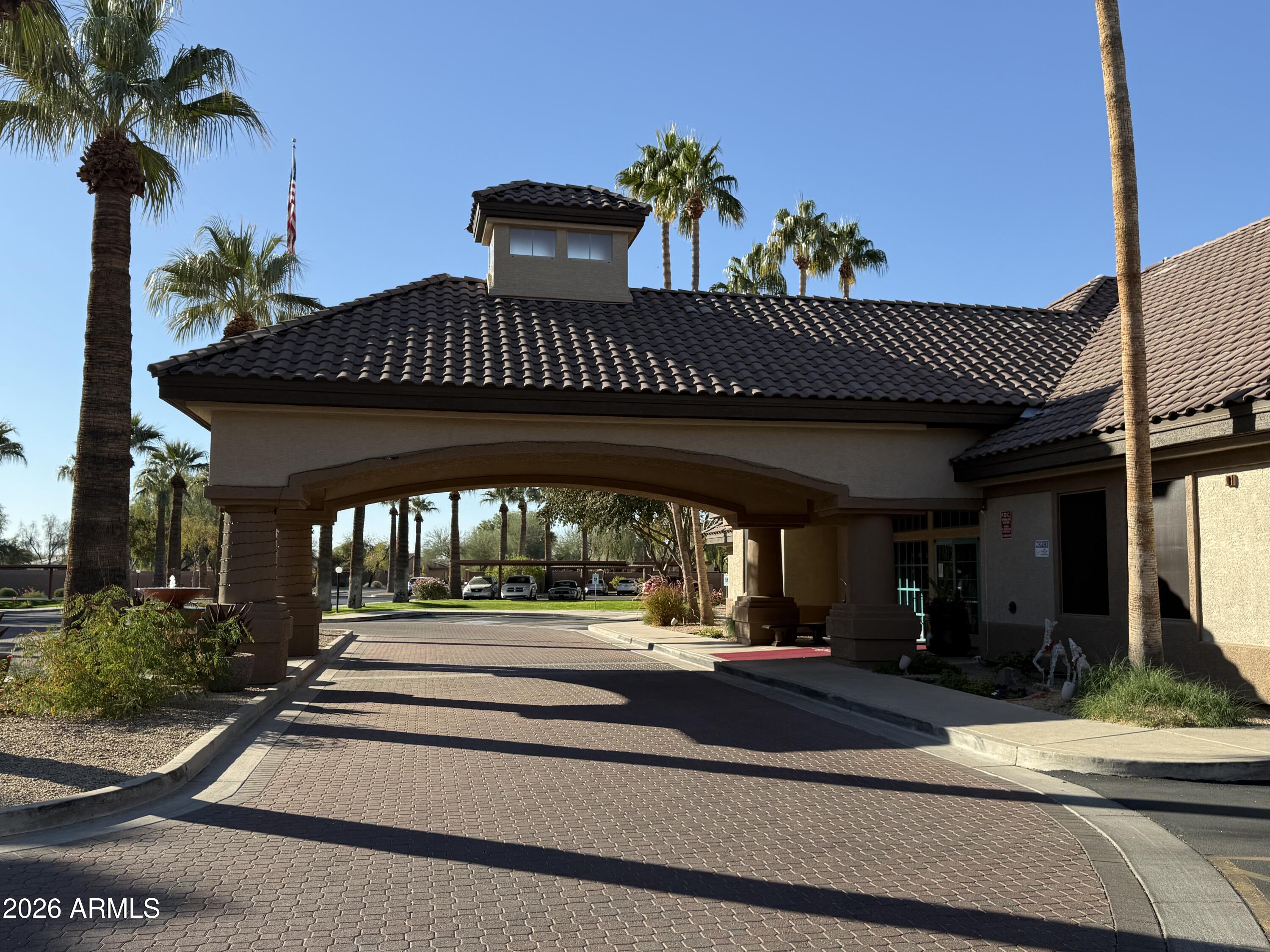 Covered entrance with a dark tile roof, brick-paved driveway, and palm trees.