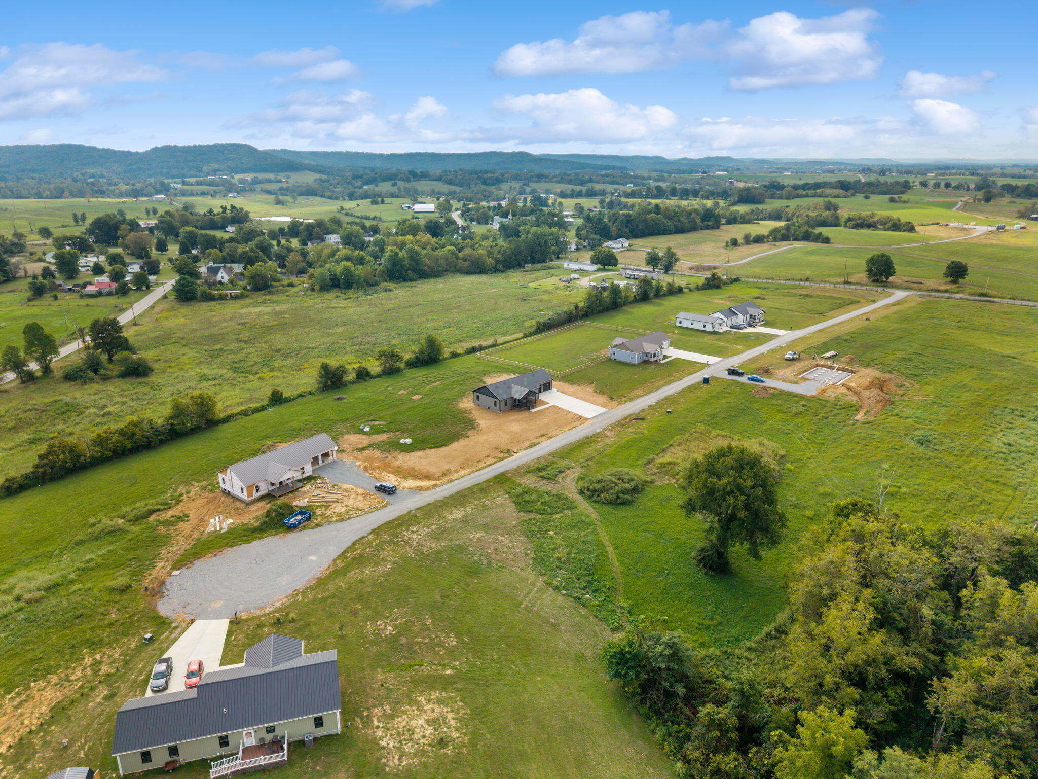 Aerial view of homes along a winding road amid open fields and wooded hills.