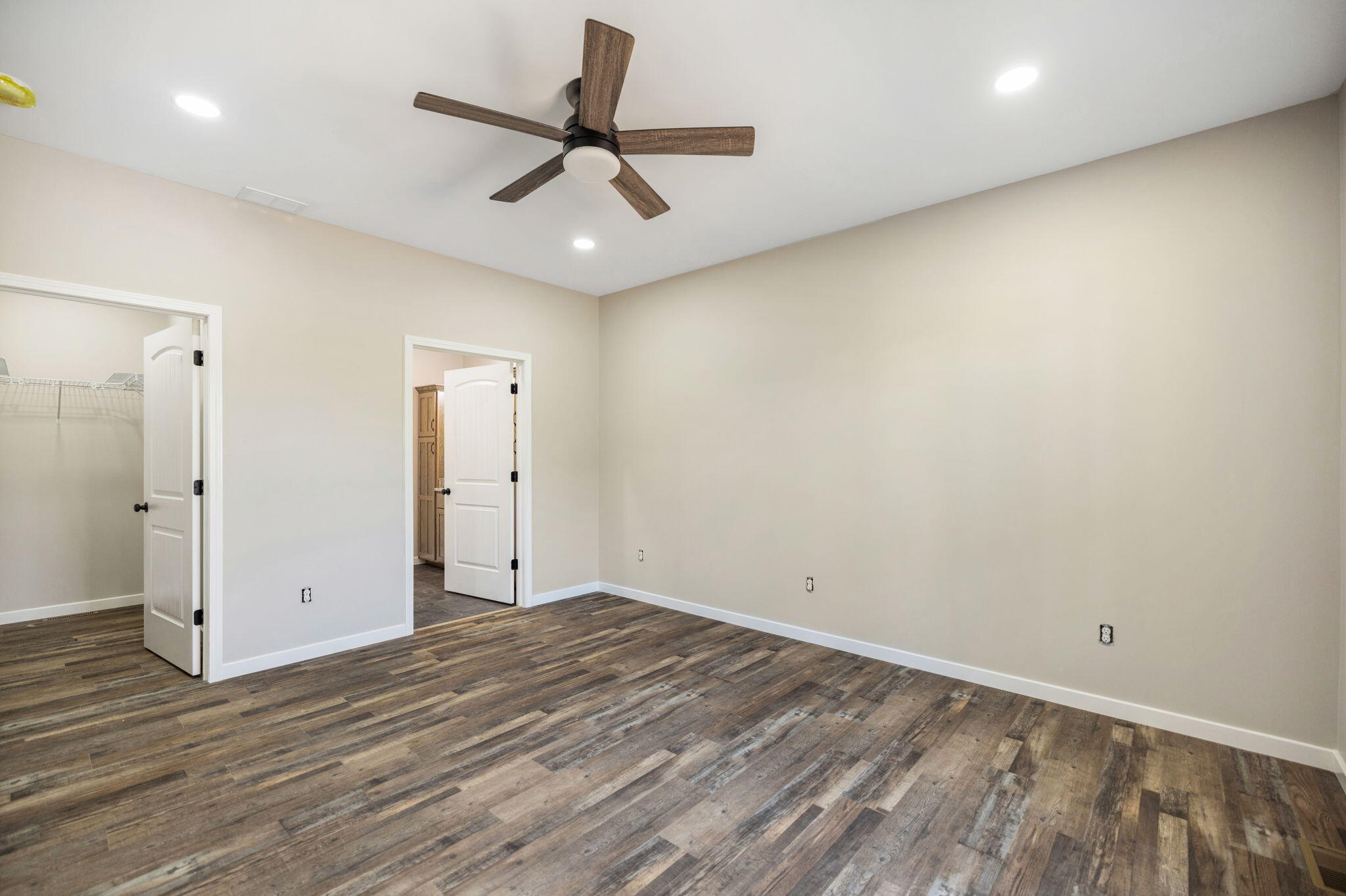 Empty bedroom with dark plank flooring, a wood-tone ceiling fan, and open doorways to a closet and adjoining room.