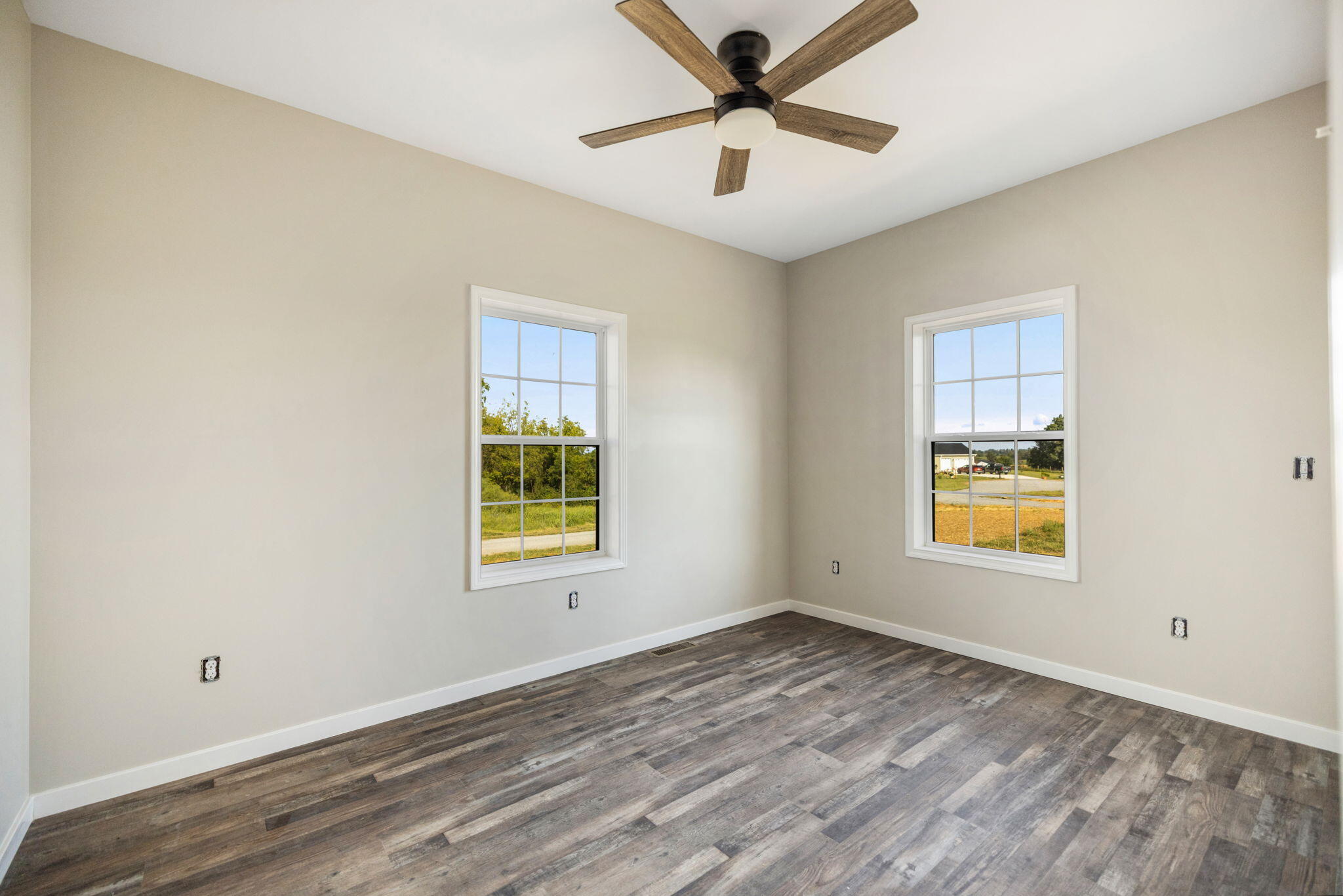 Empty bedroom with two windows, wood-look flooring, and a wood-blade ceiling fan.