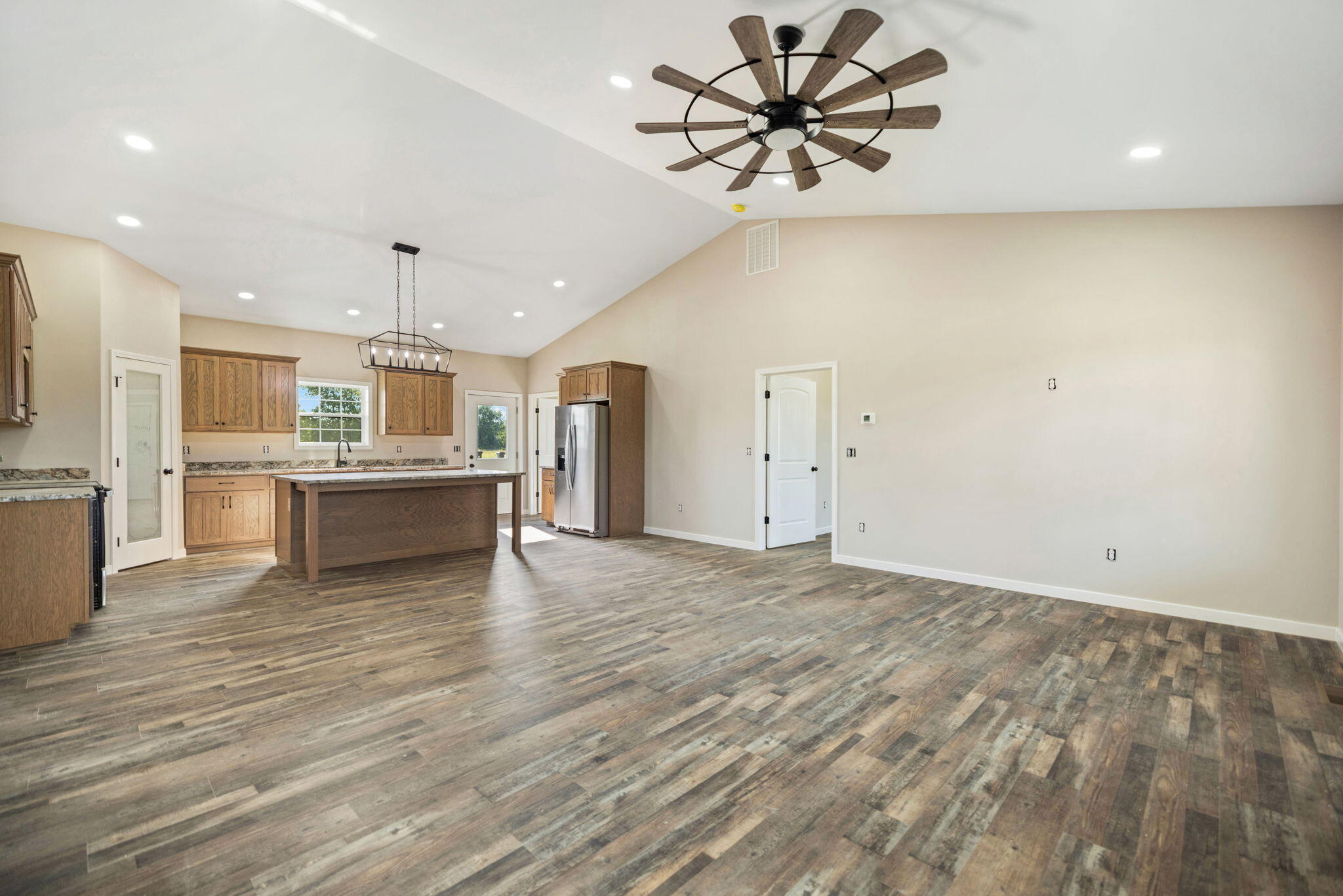 Open kitchen with a large island, wood cabinets, stainless steel refrigerator, and high ceiling fan.