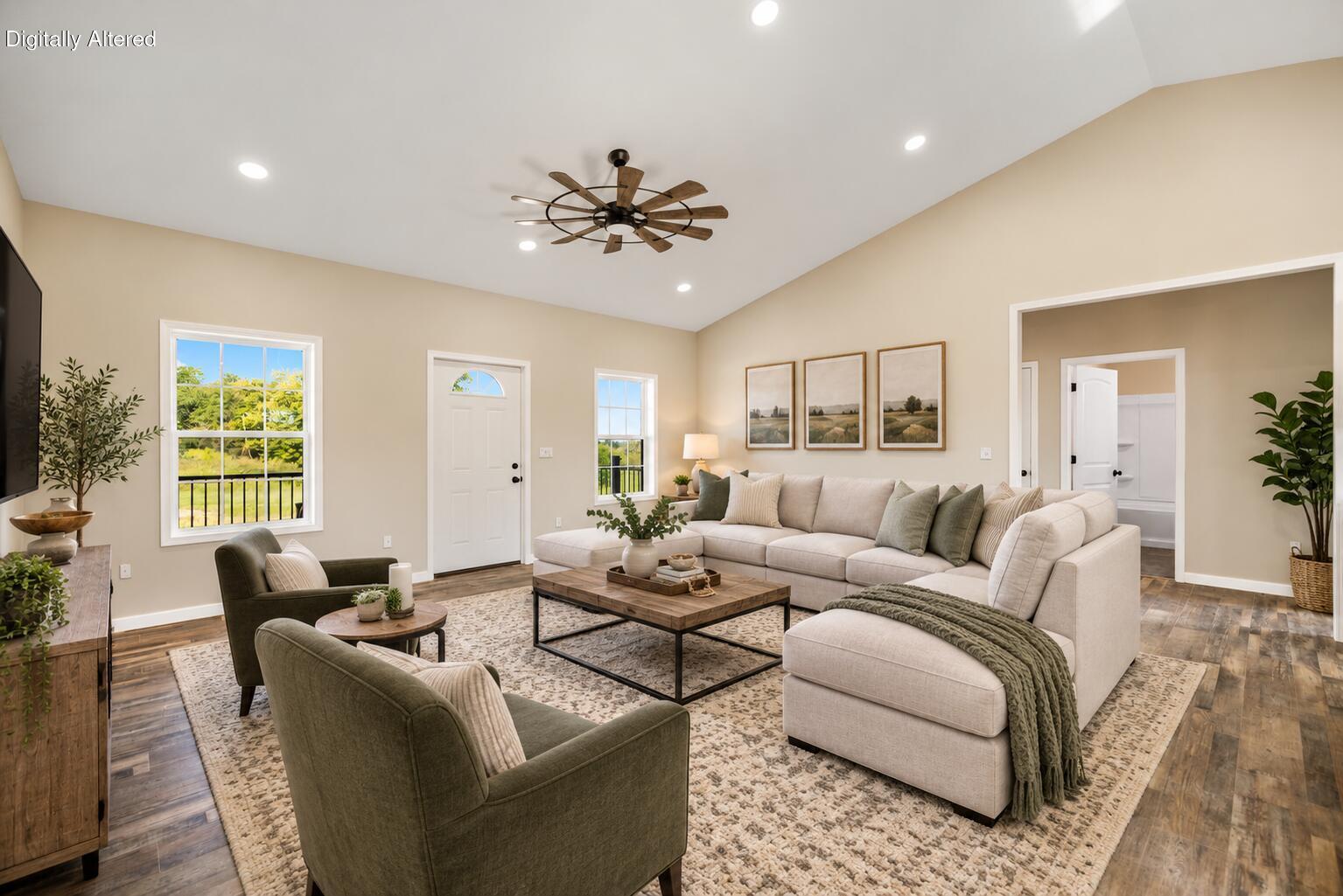Staged living room with a vaulted ceiling, cream sectional, and windows overlooking greenery.
